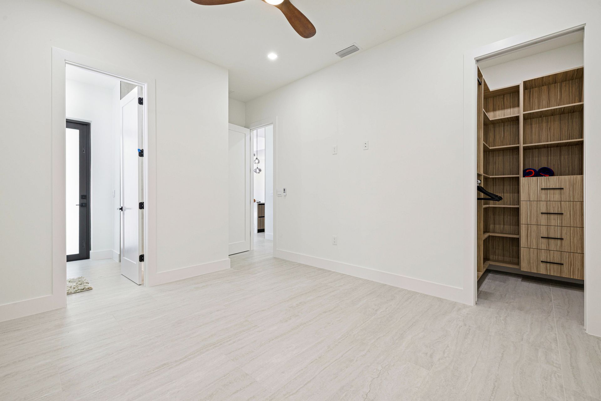 Empty bedroom with white walls and flooring, walk-in closet, and open doorways.