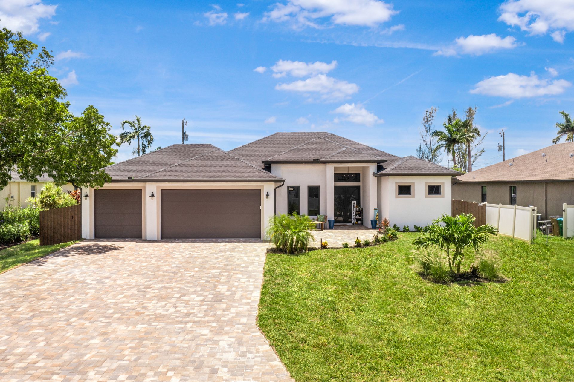Modern single-story house with beige exterior, brown roof, and two-car garage on a sunny day.