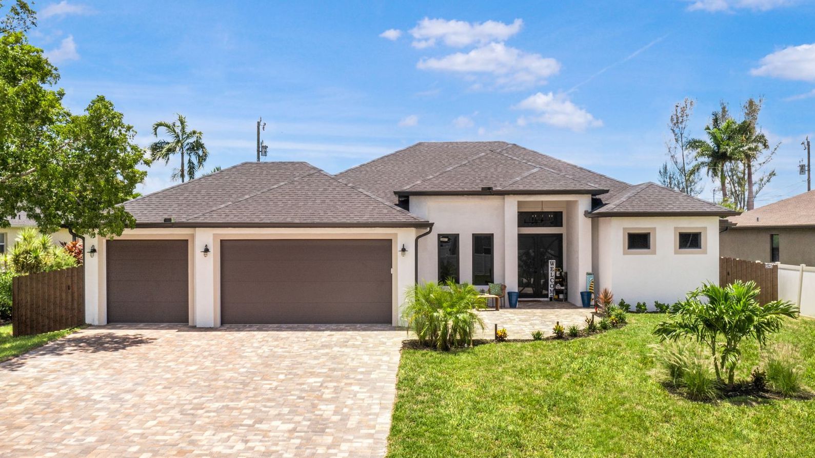 Modern white house with brown garage doors and a brick driveway under a blue sky.