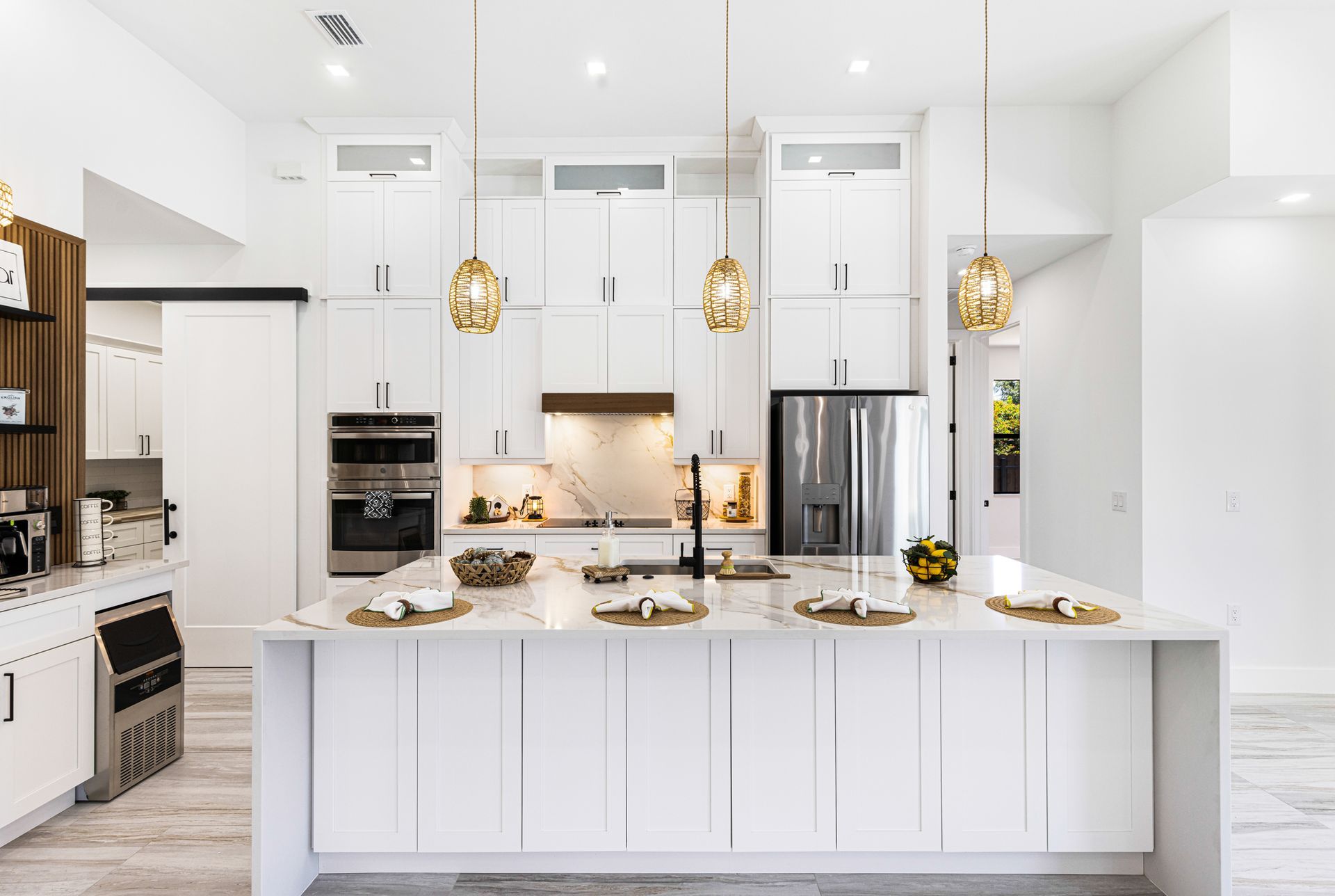 Modern white kitchen with large island, gold pendant lights, and stainless steel appliances.