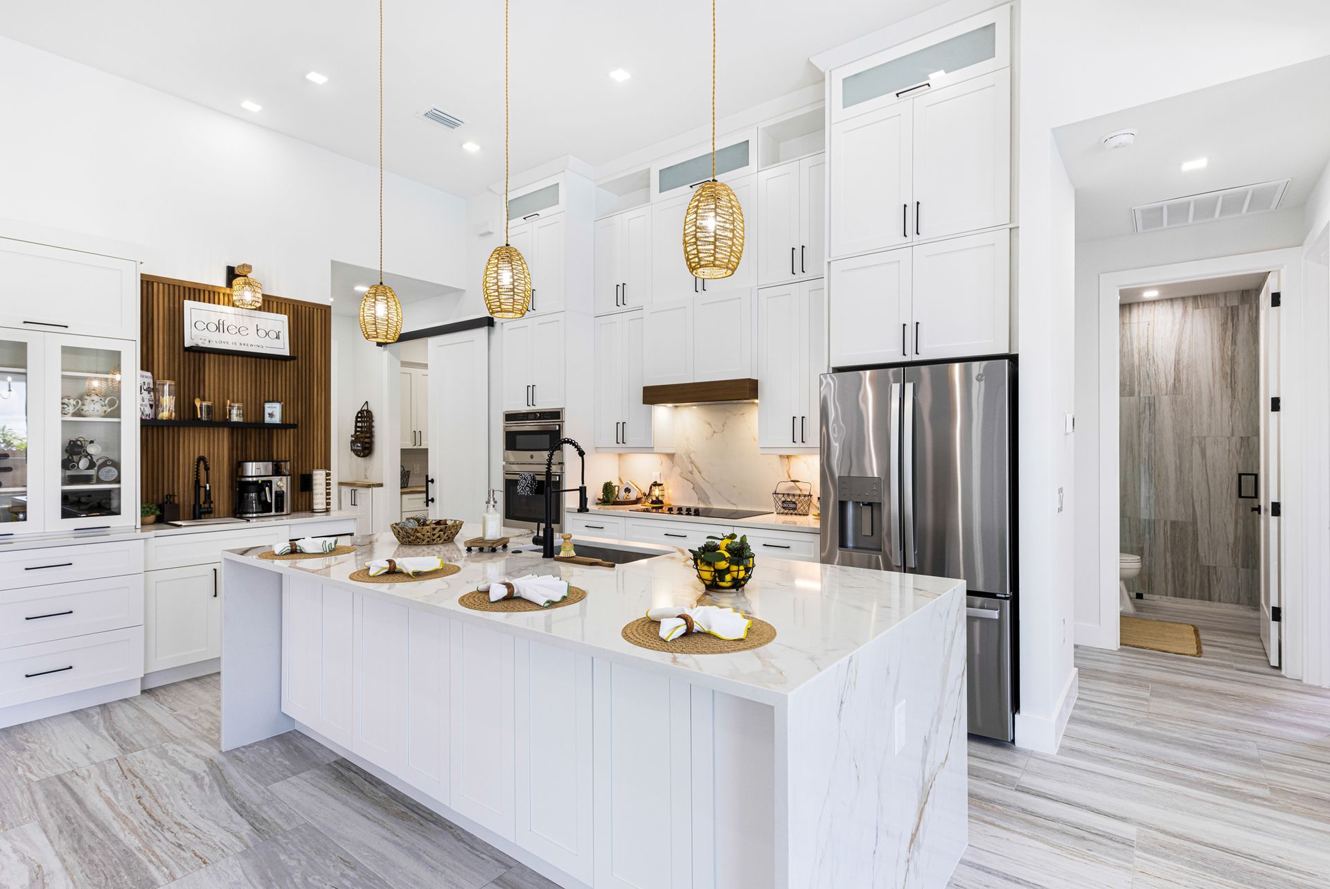 Modern white kitchen with island, stainless steel appliances, and gold pendant lights.