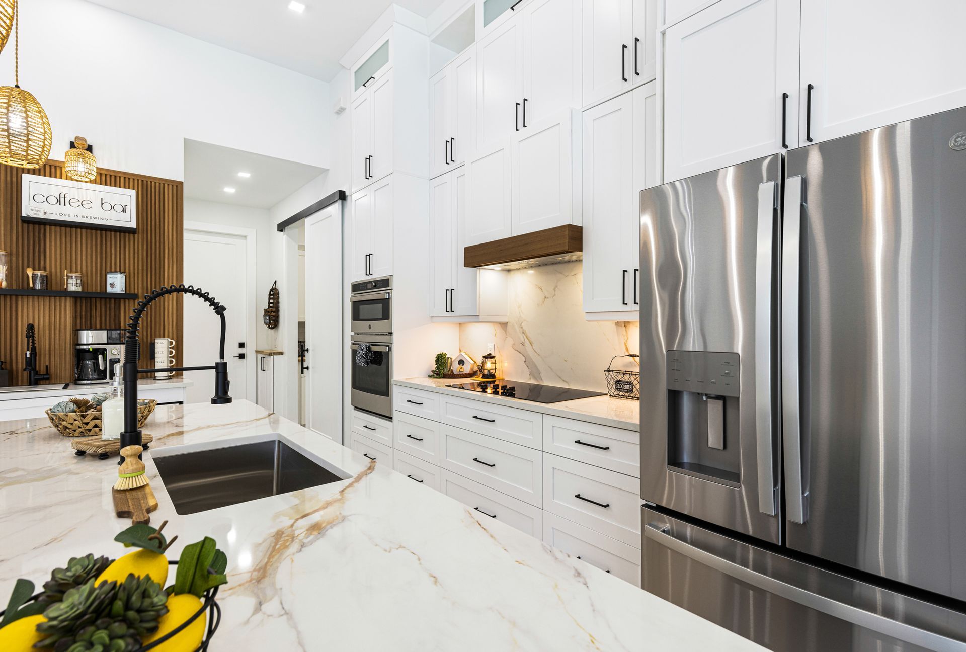 Modern white kitchen with stainless steel appliances, marble countertops, and dark accents.