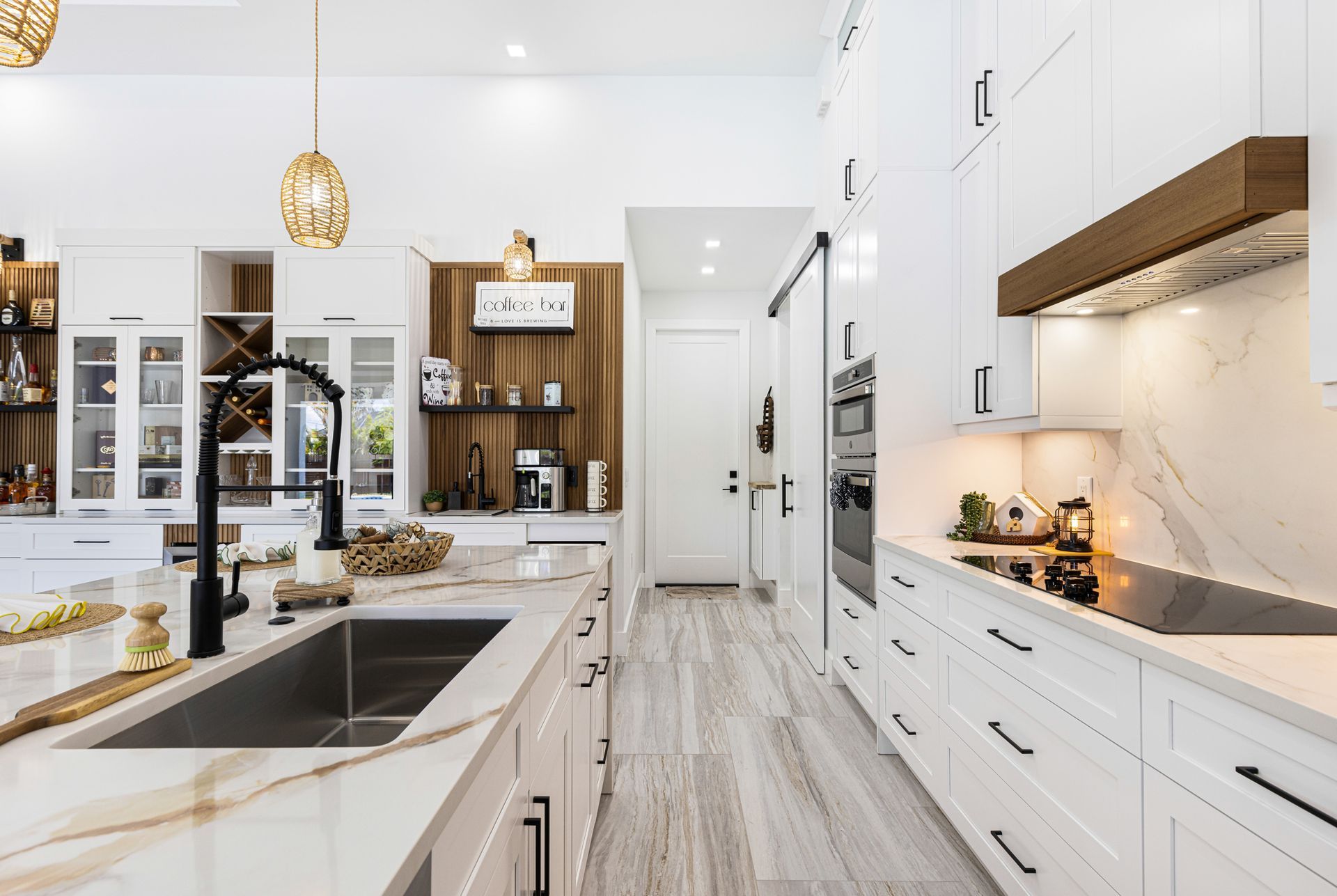 Modern white kitchen with marble countertops, black fixtures, and wooden accents.
