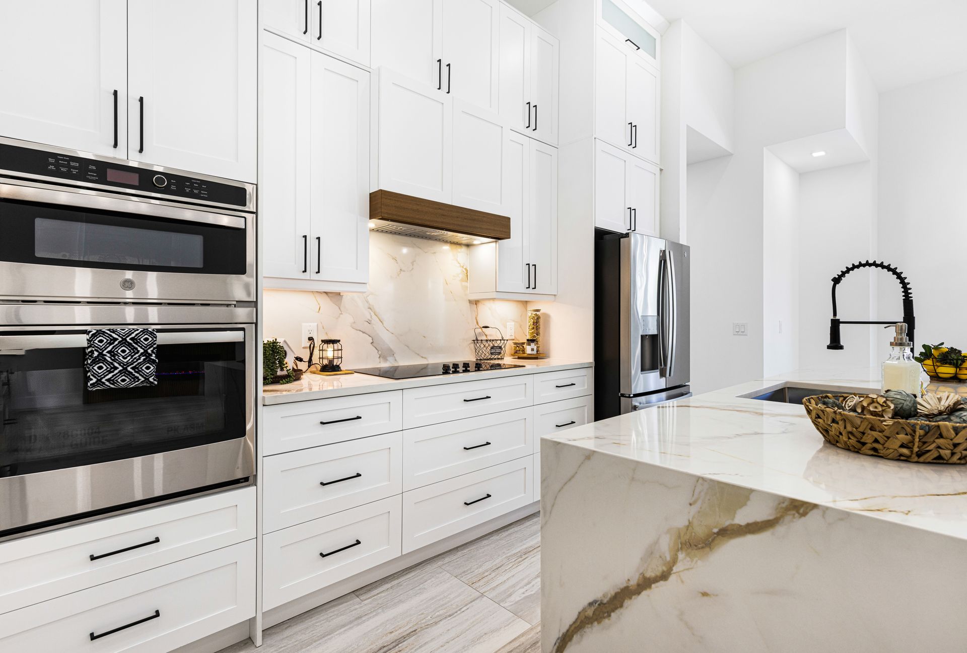 Modern white kitchen with marble island and countertops, stainless steel appliances, and black accents.