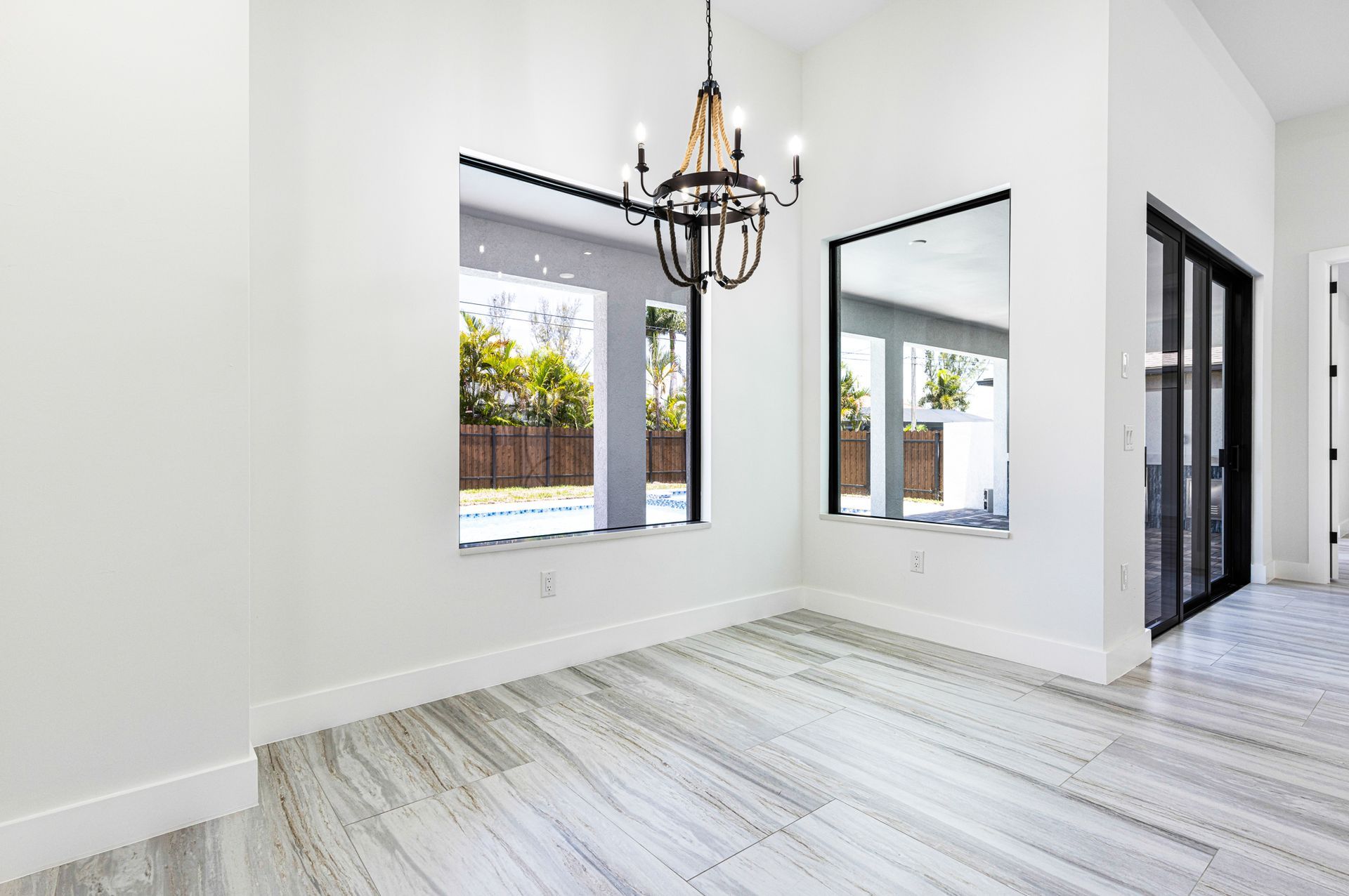 Bright dining room with marble-look floors, large windows, and a black chandelier.