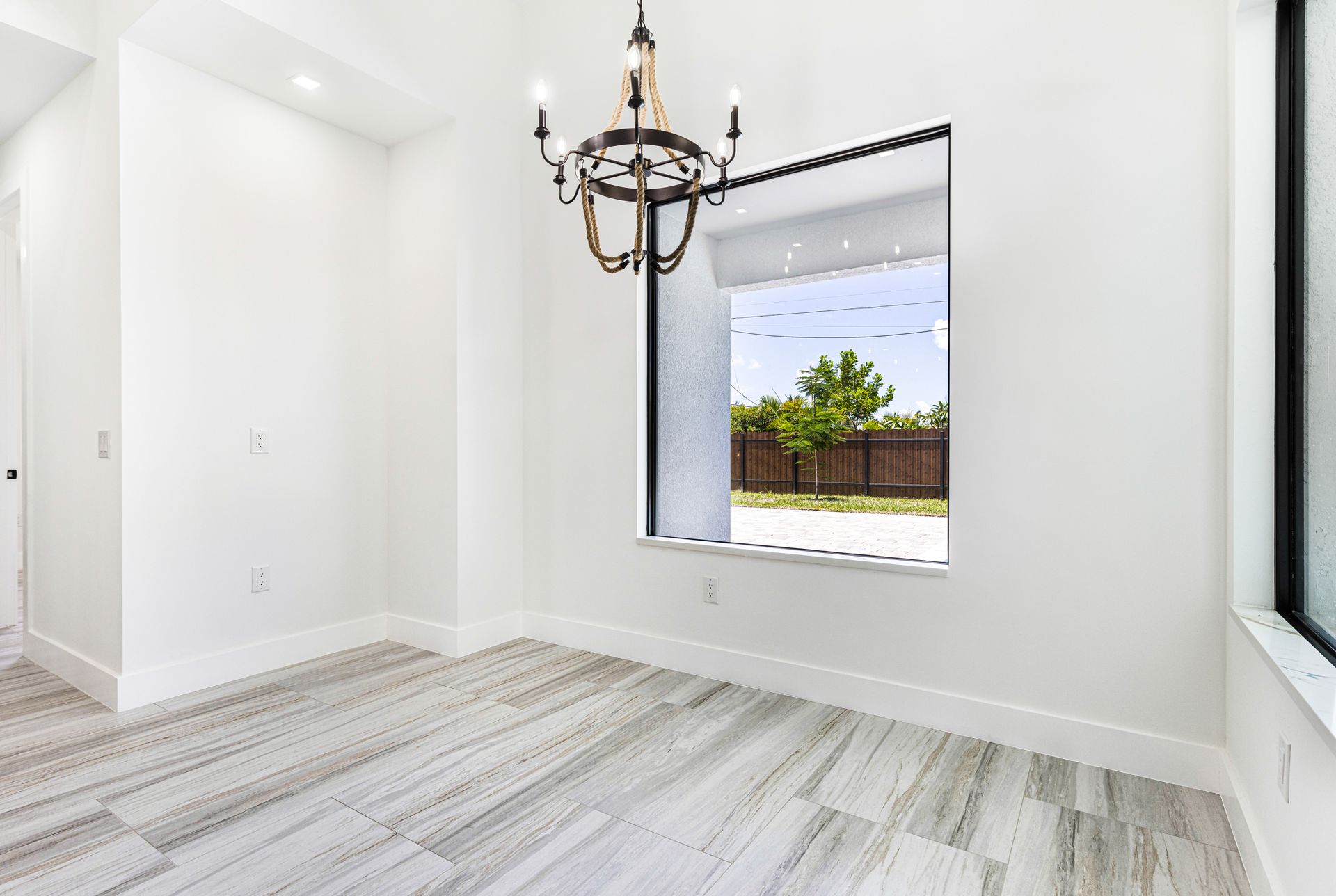 Empty room with light wood-look flooring, white walls, large window, and chandelier.