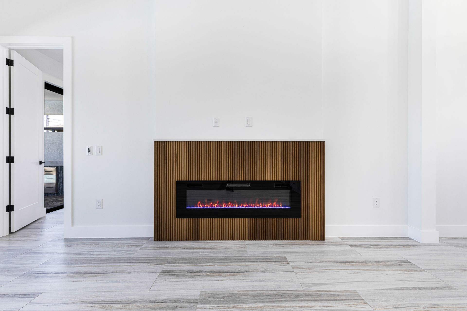 Electric fireplace with orange flames on a wooden accent wall in a white room.