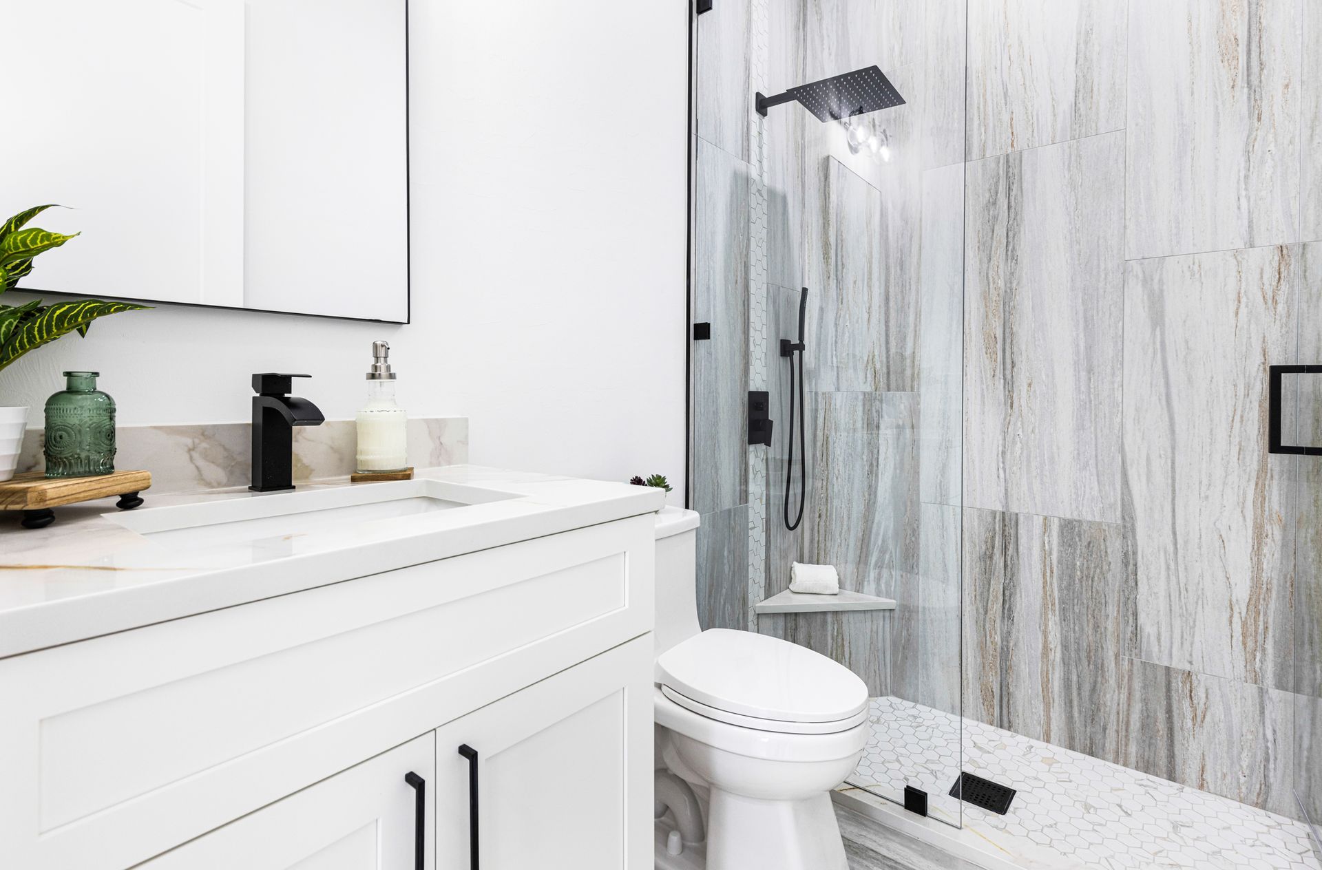 Modern bathroom with white vanity, toilet, and glass shower with patterned tile.