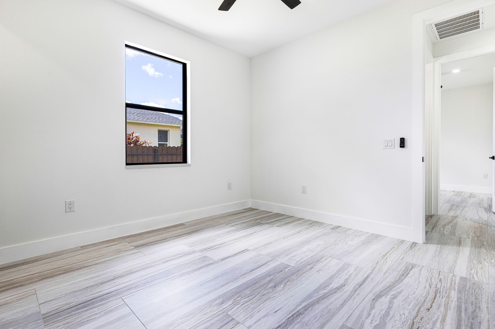 Empty white bedroom with wood-look floor, window, and doorway.