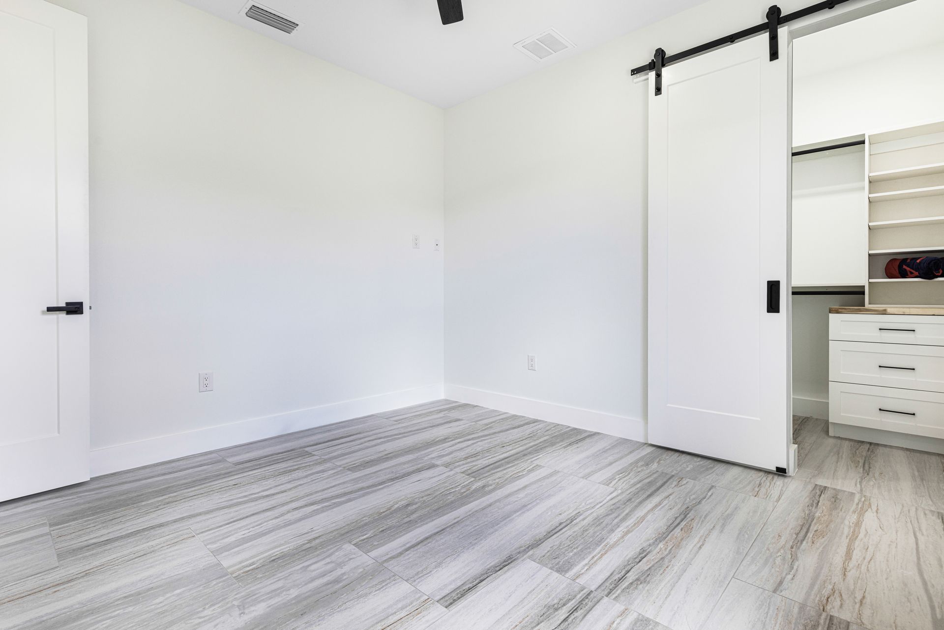 Empty room with light gray flooring, white walls, and a sliding barn door leading to a closet.