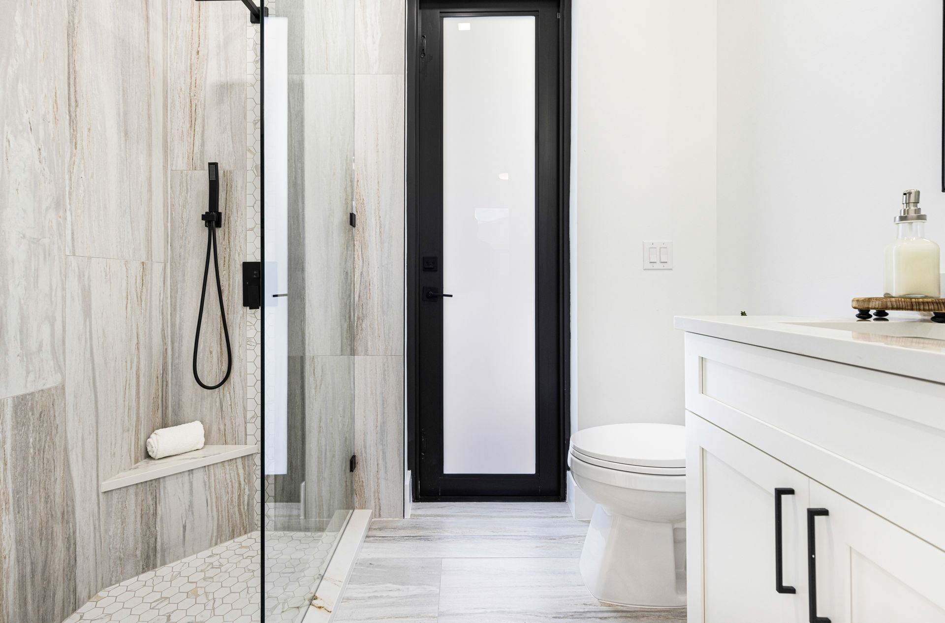 Bathroom with a marble shower, black framed door, white cabinets, and toilet.