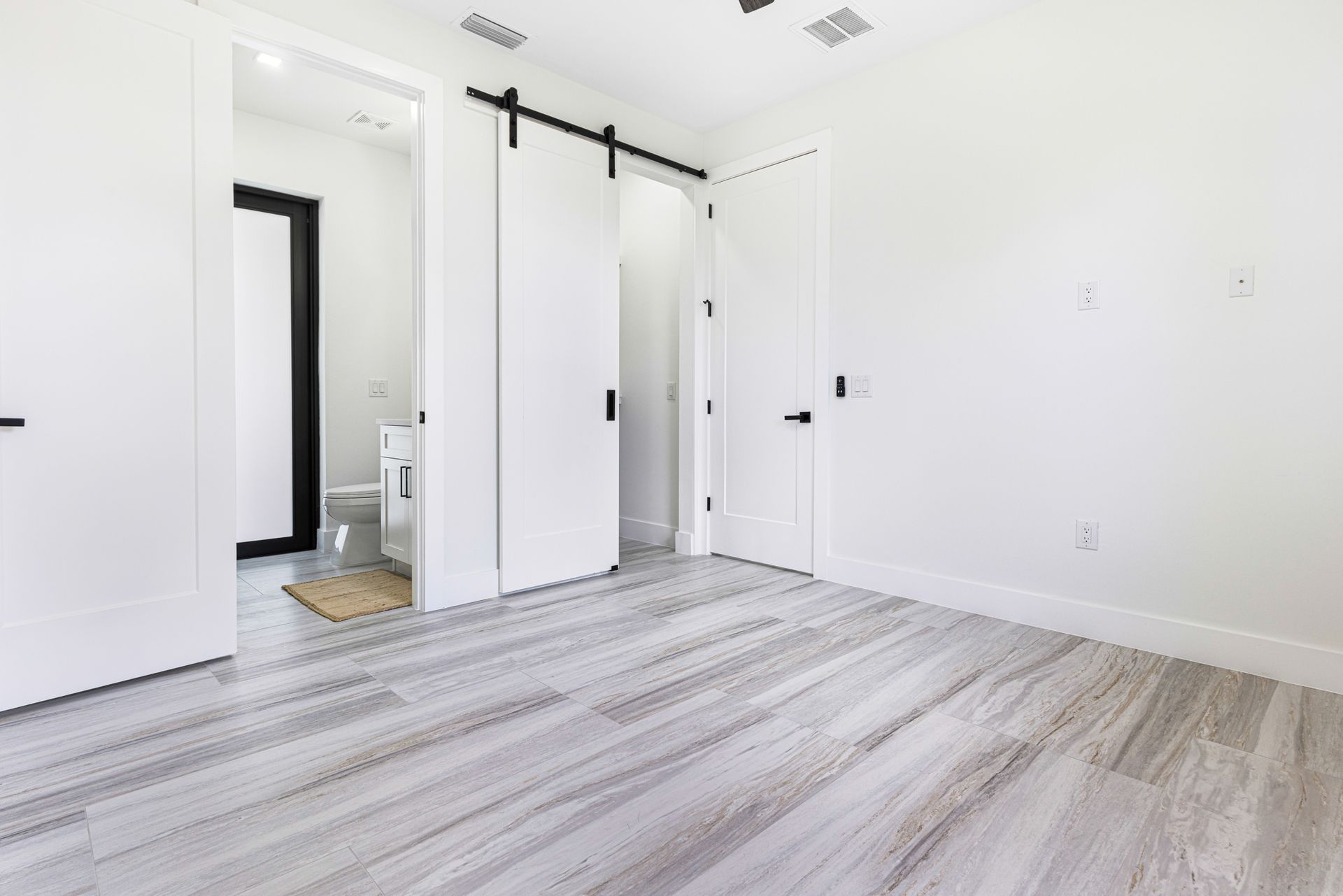 Empty bedroom with light grey wood-look flooring, white walls, and black door hardware.