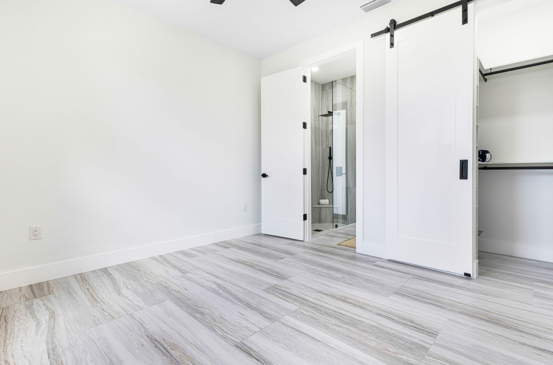 Empty bedroom with light gray wood-look flooring, white walls, and open closet and bathroom doors.