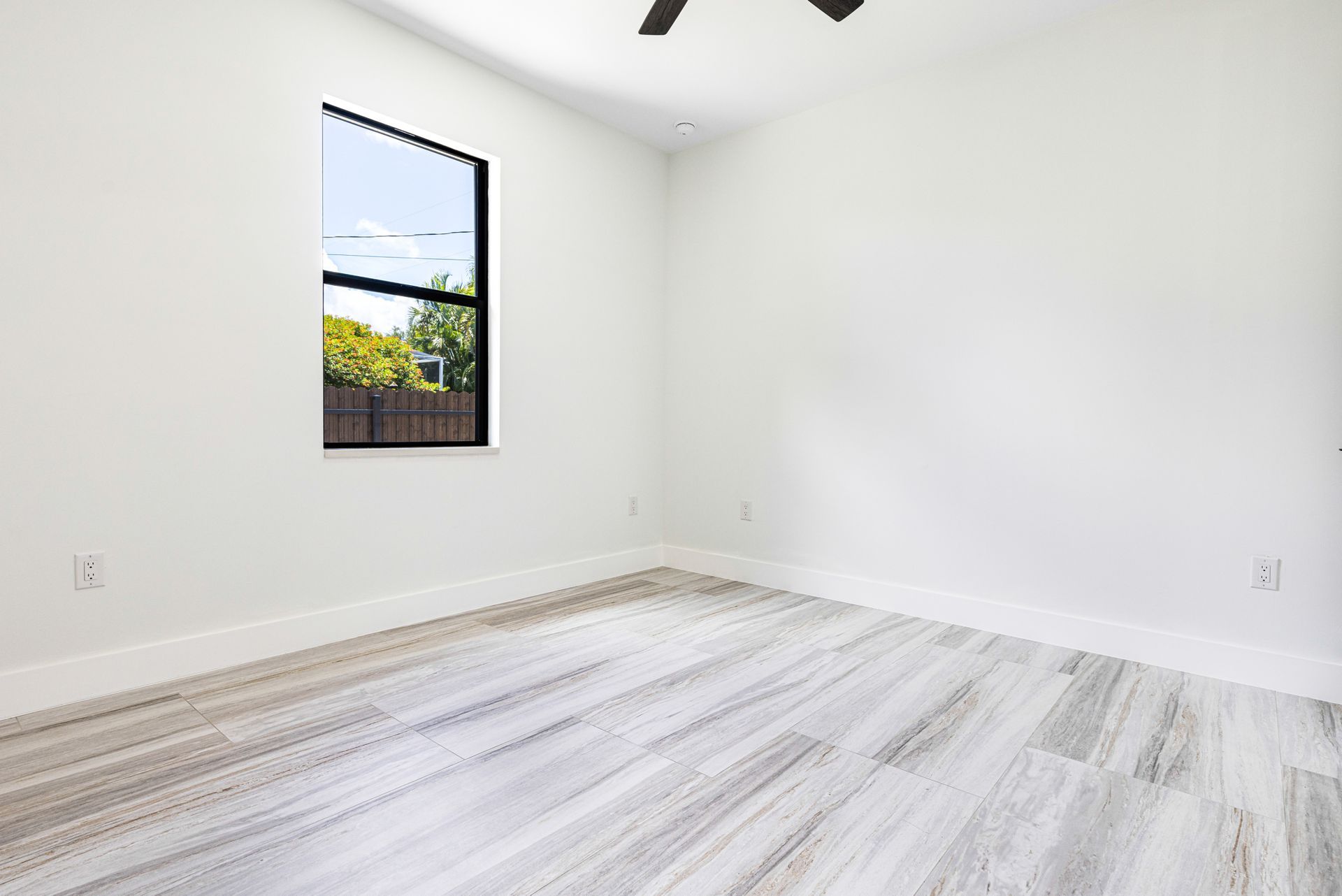 Empty room with light grey wood-look flooring, white walls, and a window with an outdoor view.