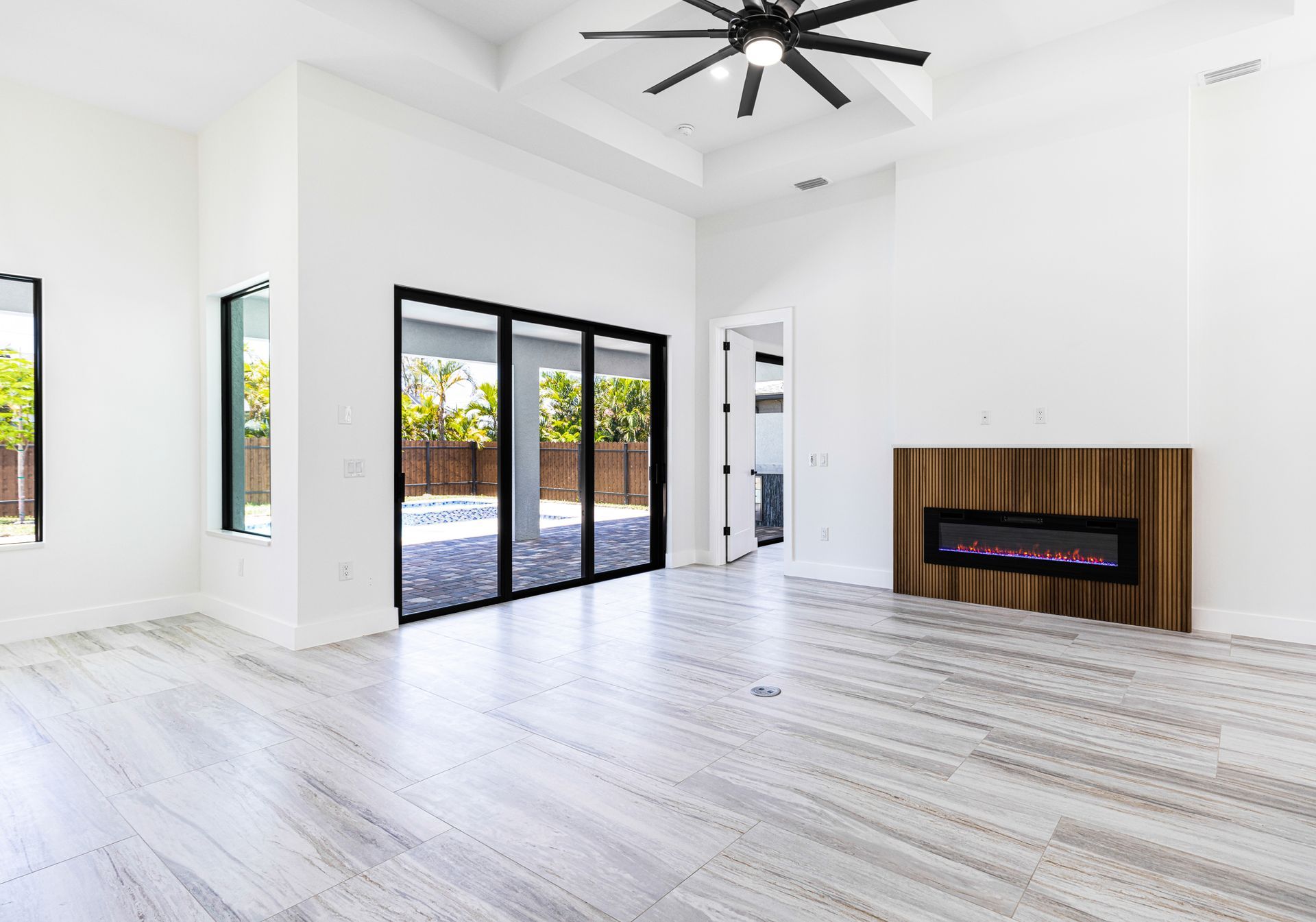 Spacious, bright room with a fireplace, sliding glass doors to a pool area, and light-colored wood floors.