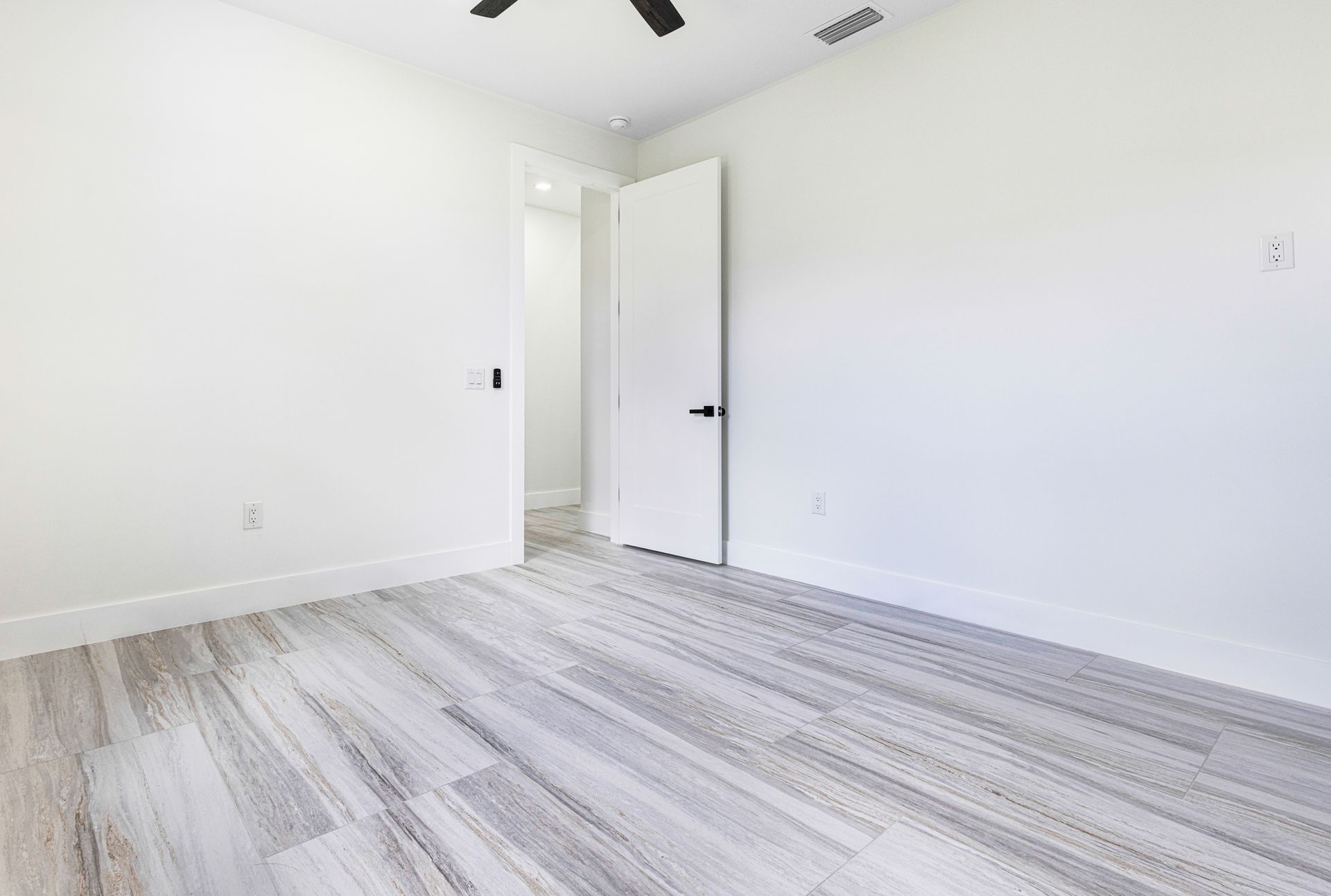 Empty white bedroom with wood-look floor, doorway to another room.