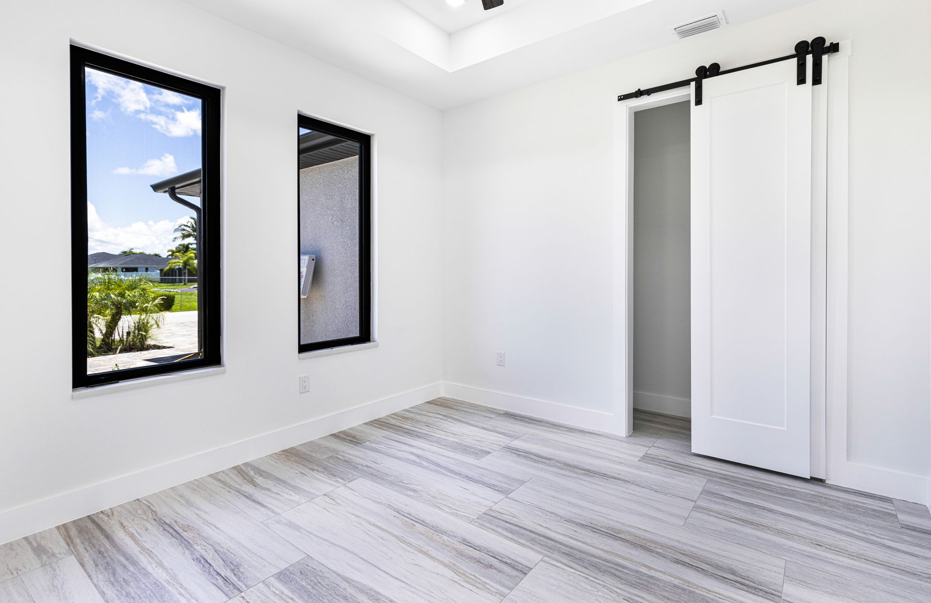 Empty, white room with two black-framed windows and a sliding barn door, light wood-look floor.