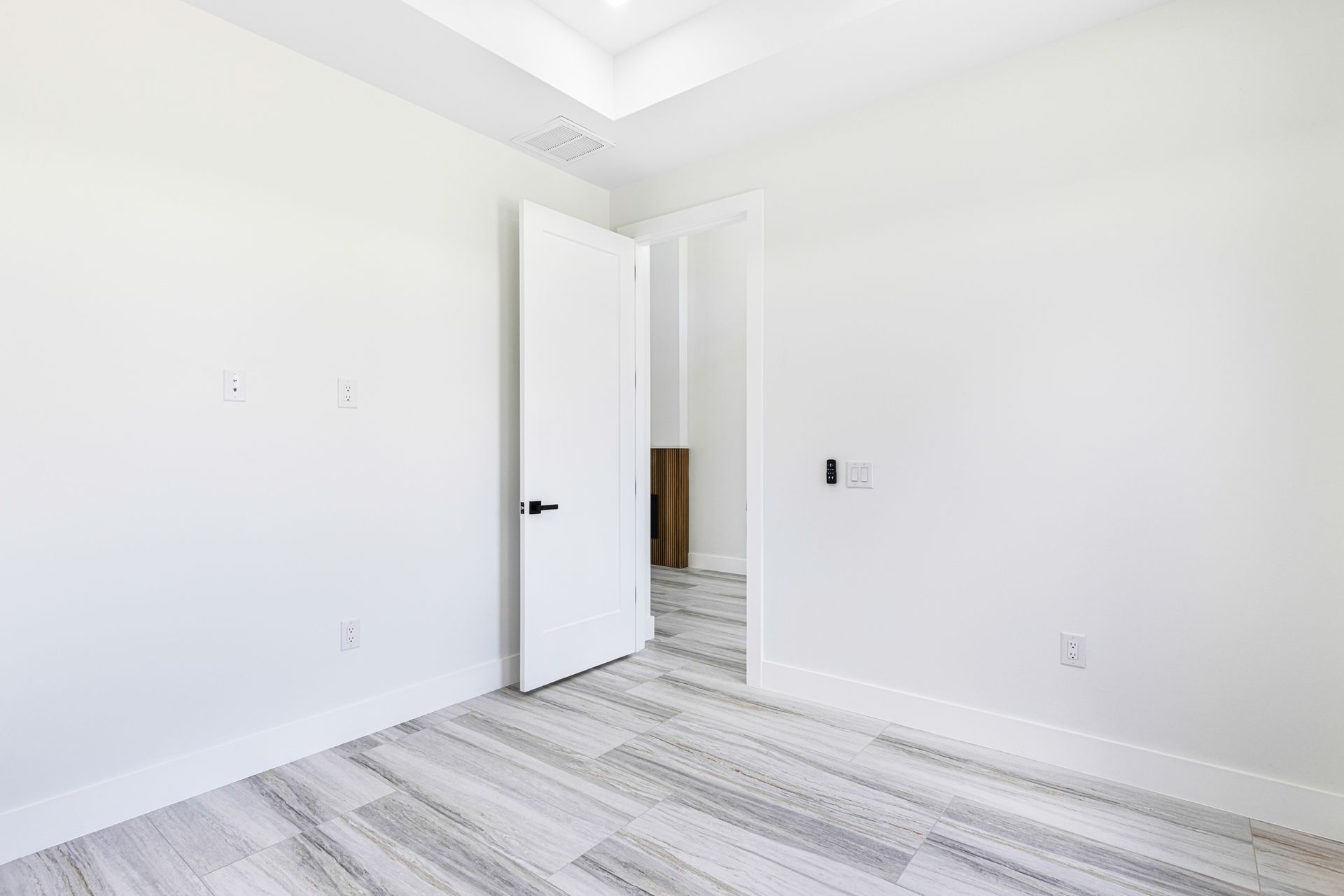 Empty white room with open door, wood-look flooring, white walls, and black doorknob.