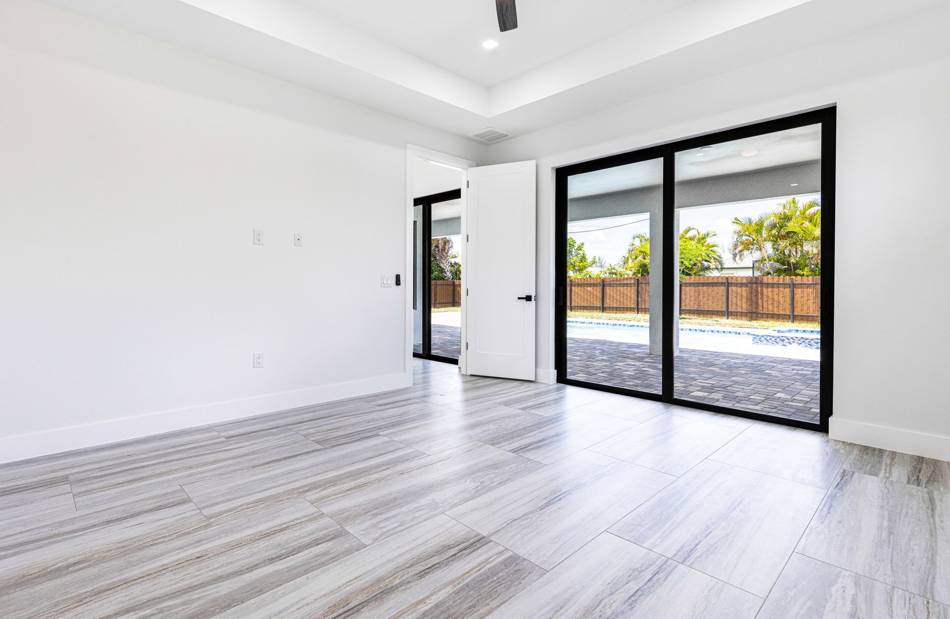Empty room with light wood-look floors, white walls, and large sliding glass doors overlooking a pool.