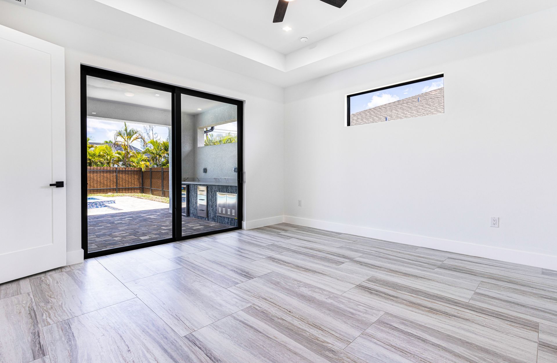 Empty bedroom with sliding glass door and small window; light wood-look flooring.