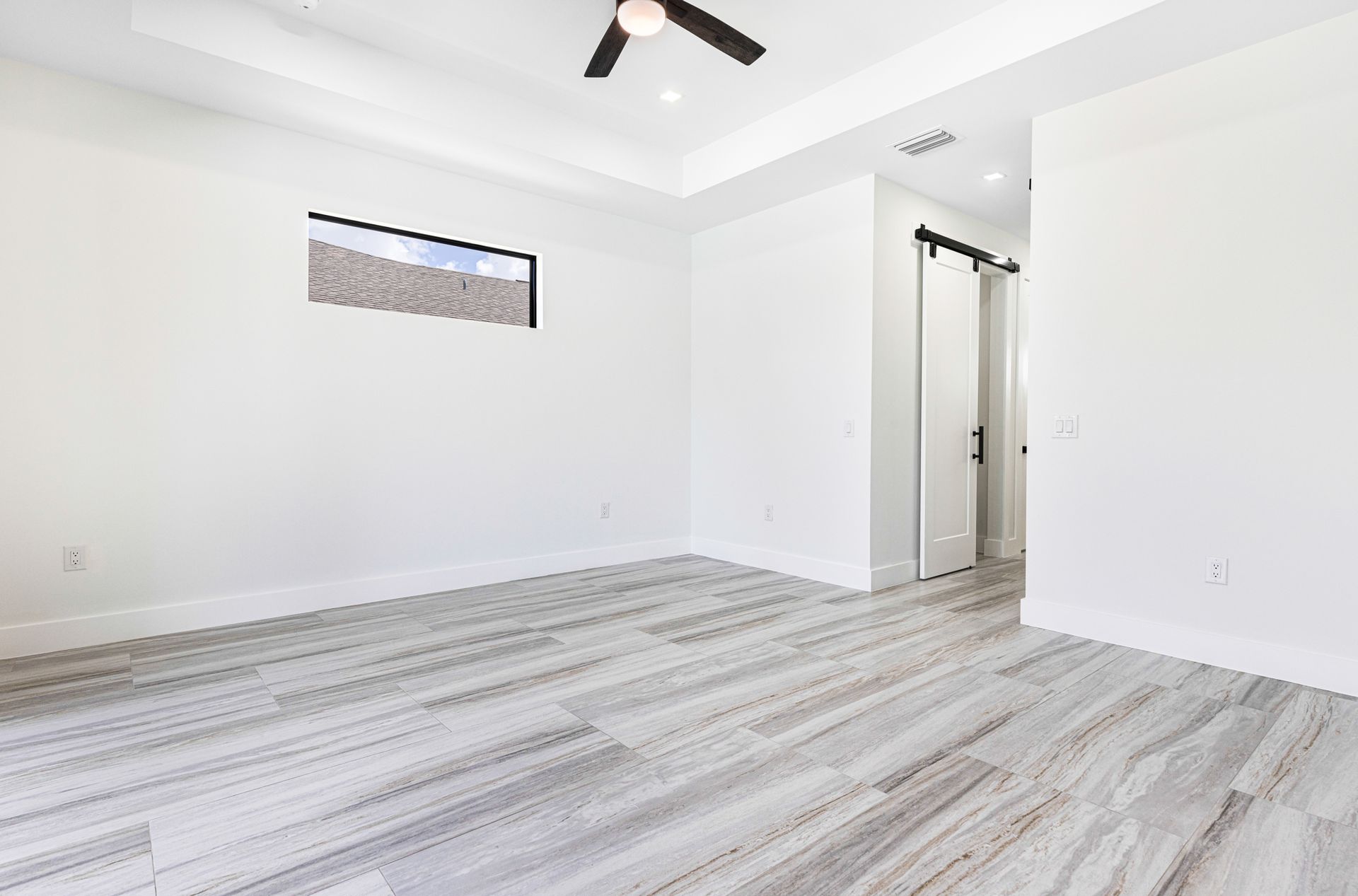 Empty bedroom with light wood-look flooring, white walls, and a barn door leading to another room.