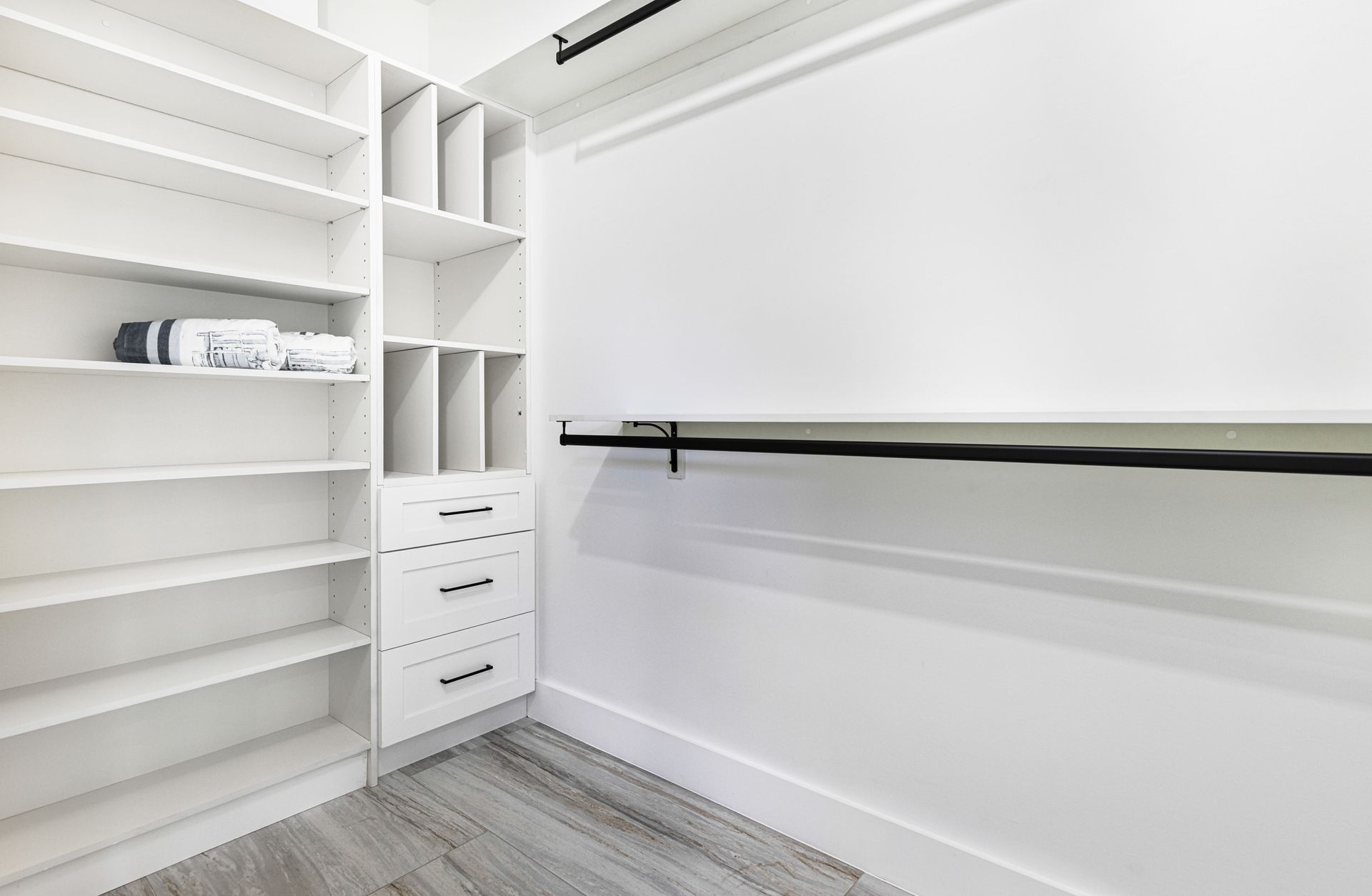 White walk-in closet with shelves, drawers, and a clothes rod, featuring a modern, minimalist design.