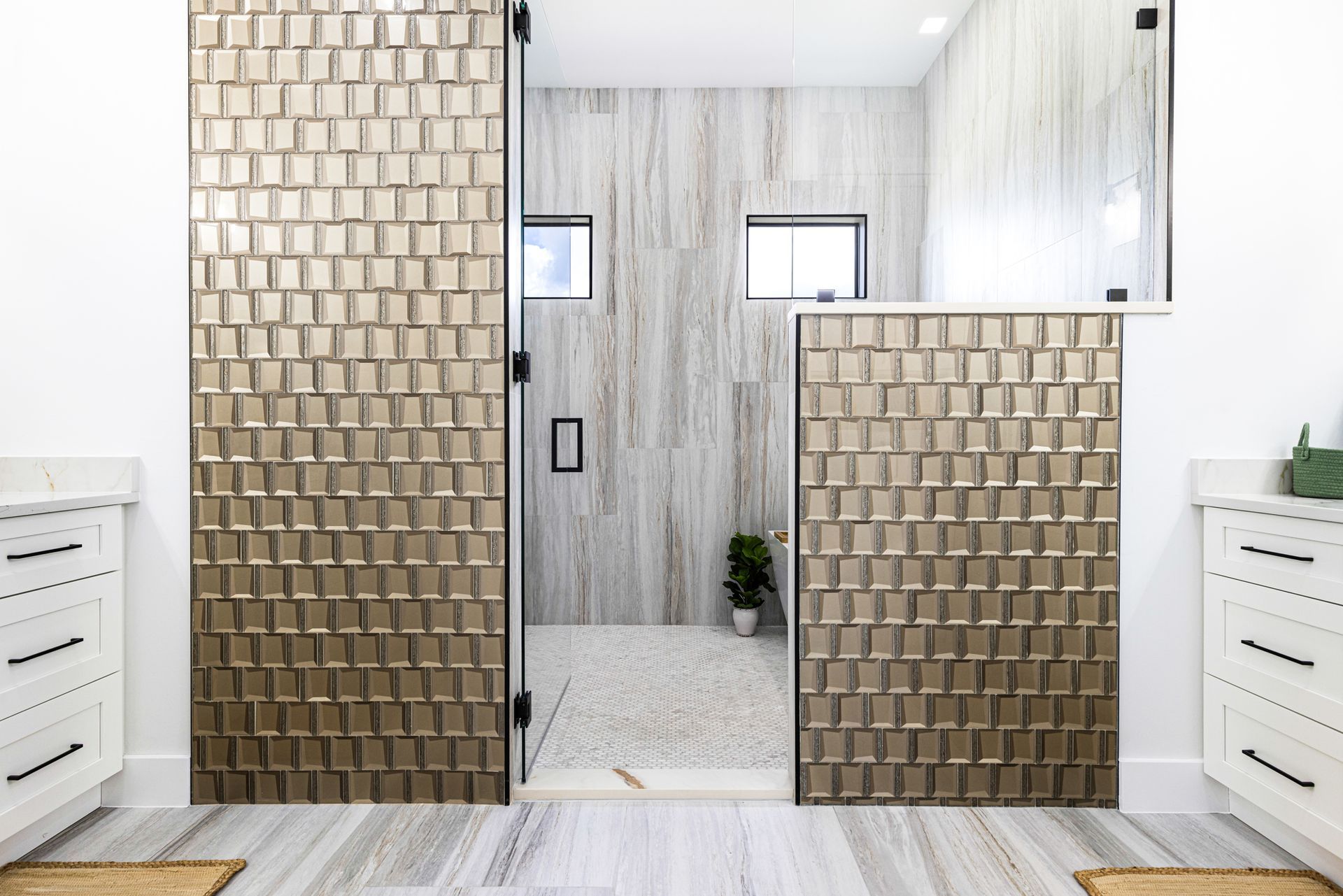 Bathroom with textured gold accent wall, glass shower, marble floor, and white cabinets.