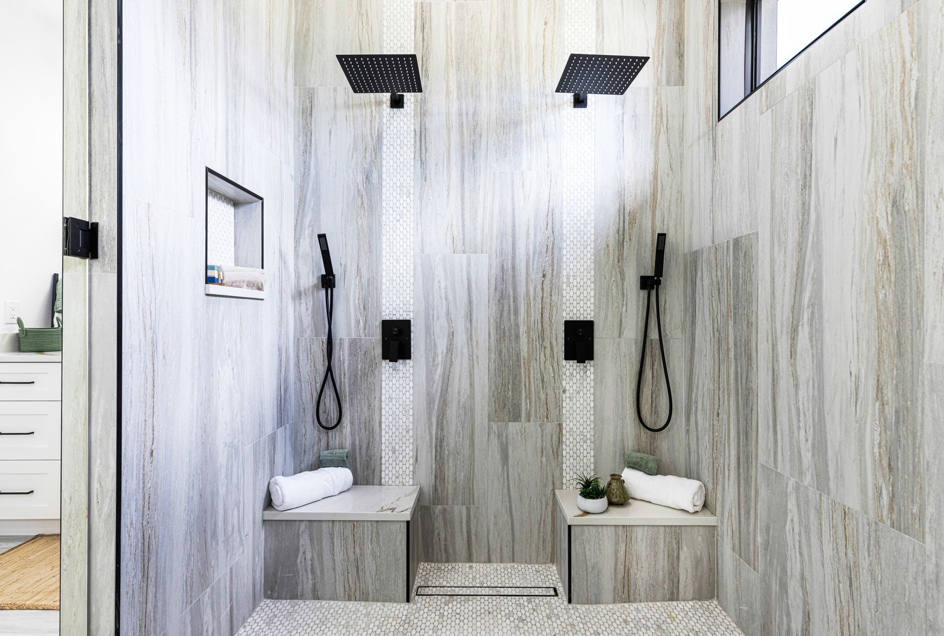 A modern, dual shower with gray and white textured walls, black fixtures, and built-in benches.