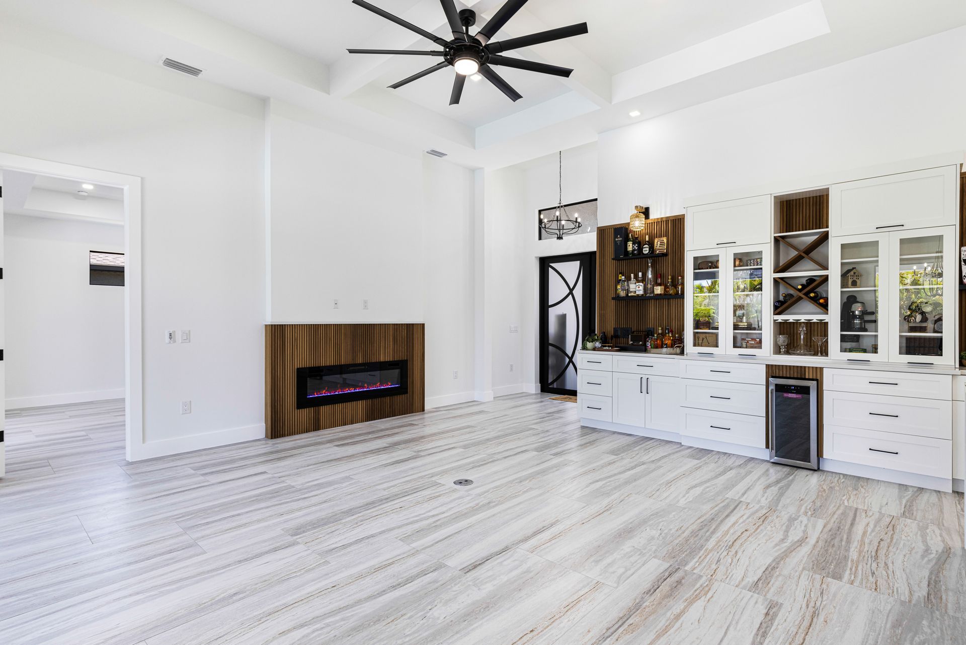 Modern living room with fireplace, bar area, white walls, wood flooring, and a black ceiling fan.