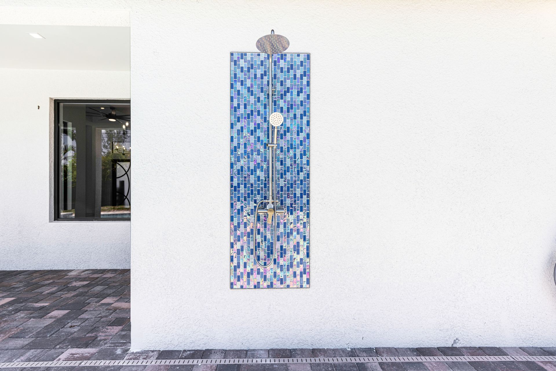 Outdoor shower with blue tile mosaic backing, chrome fixtures, on a white stucco wall.
