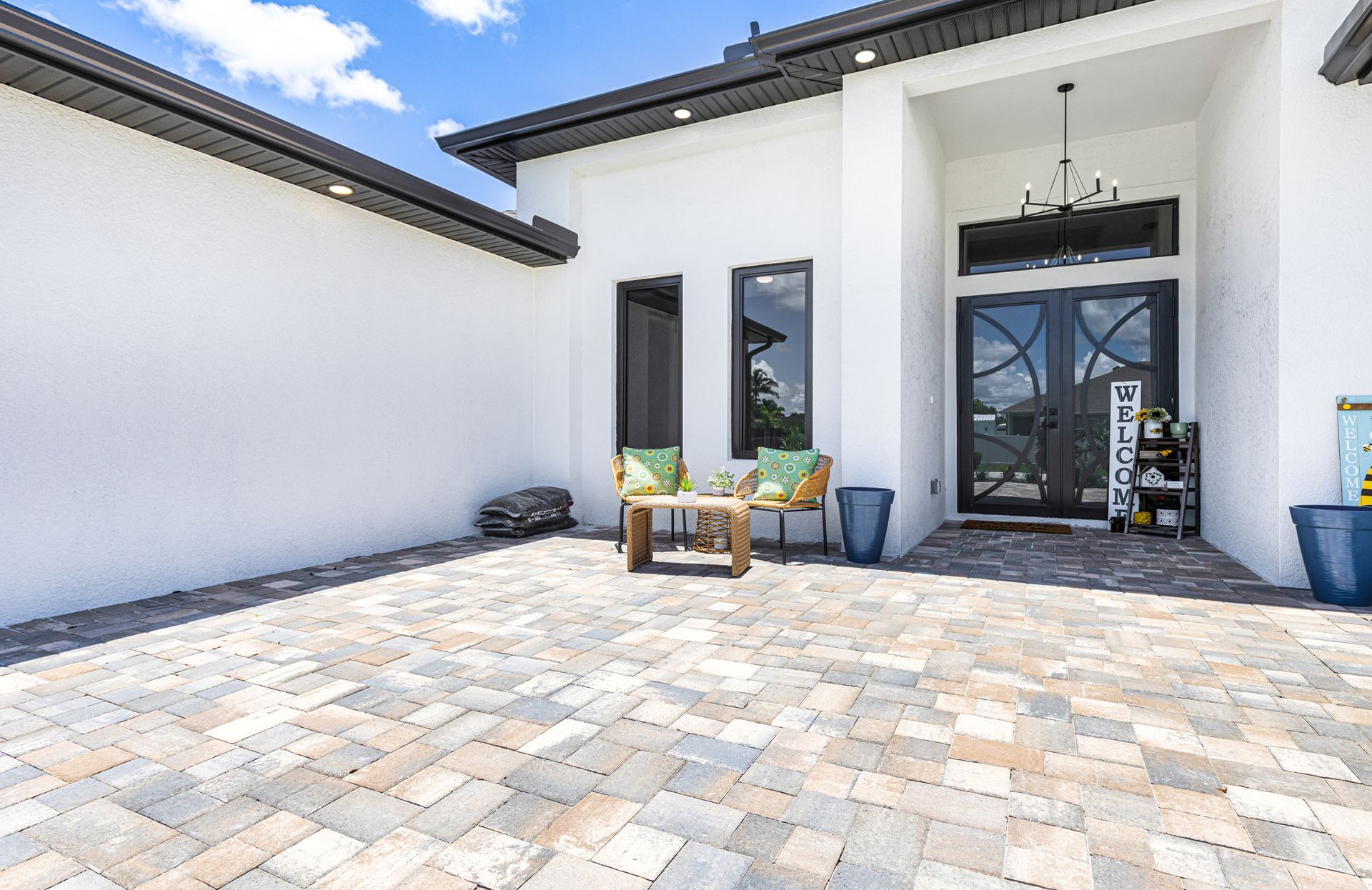 Paved patio with seating area in front of a modern white house with black double doors.