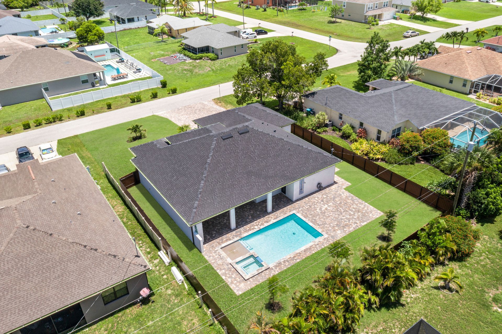 Aerial view of a house with a pool. The roof is dark, and the backyard has green grass.