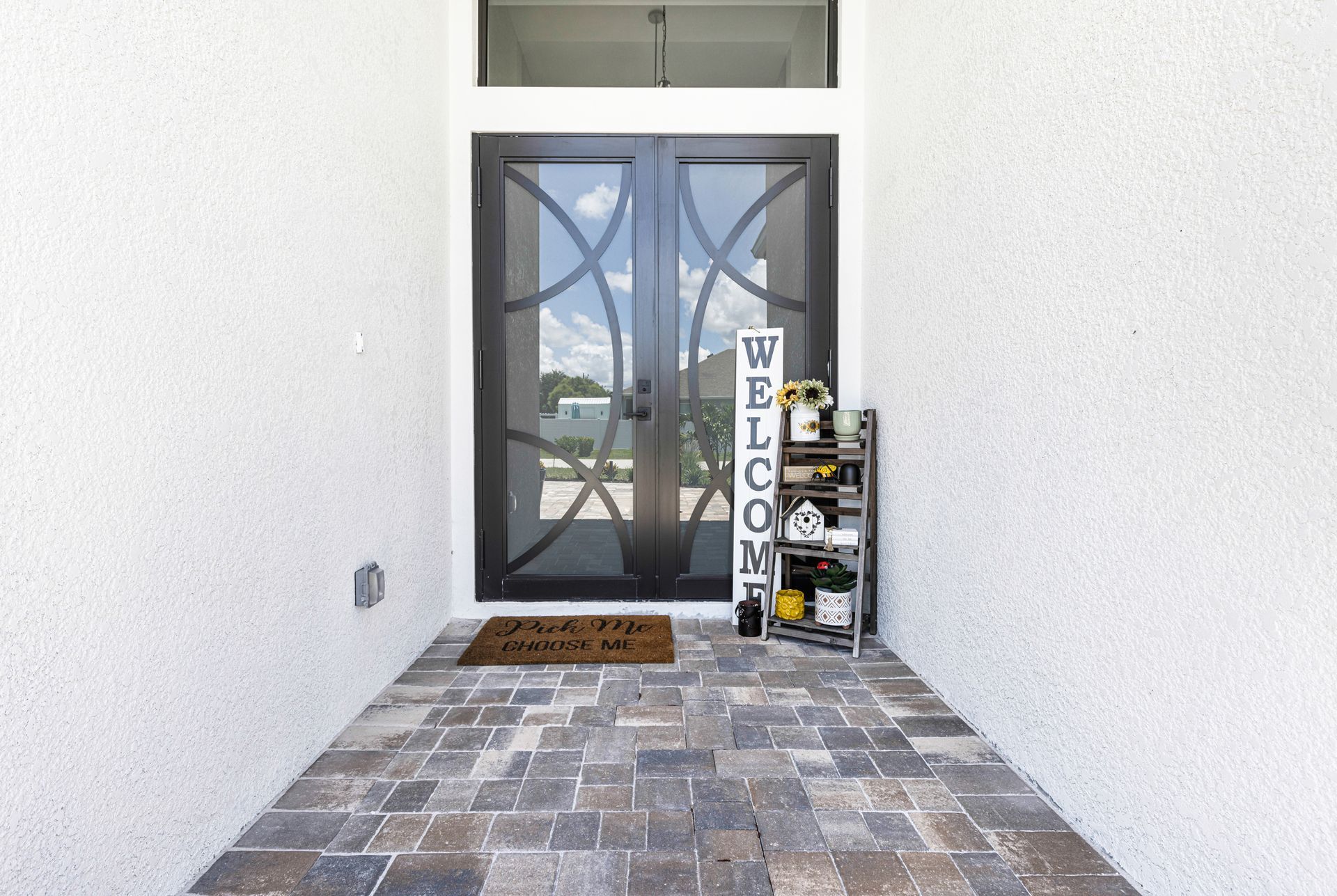 Exterior of a home with black double doors and a Welcome sign on a small shelf.