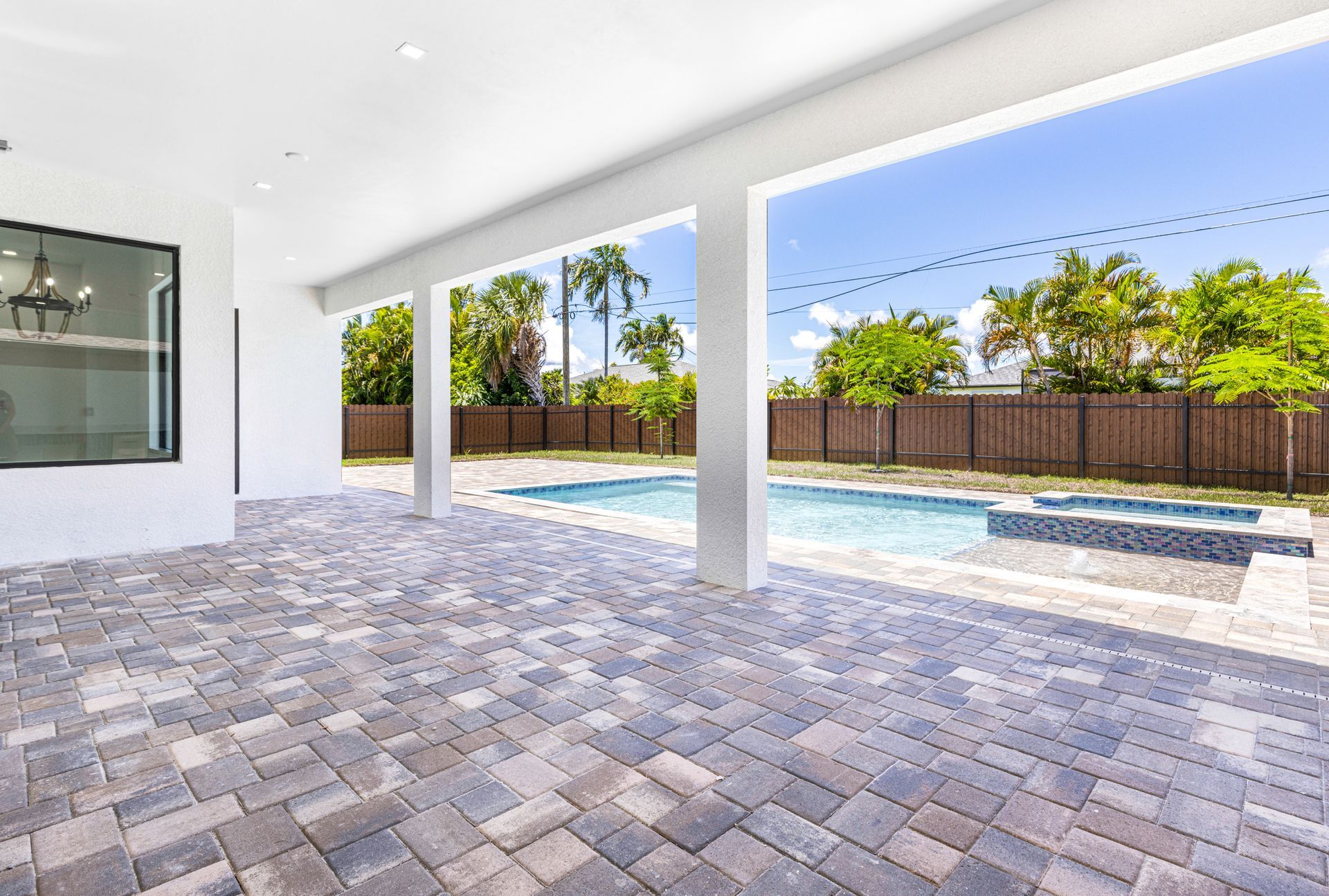 Patio overlooking a pool, with pavers and a view of trees and sky.
