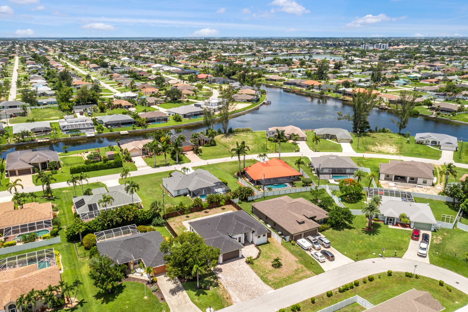 Aerial view of suburban homes with canals and lush greenery on a sunny day.