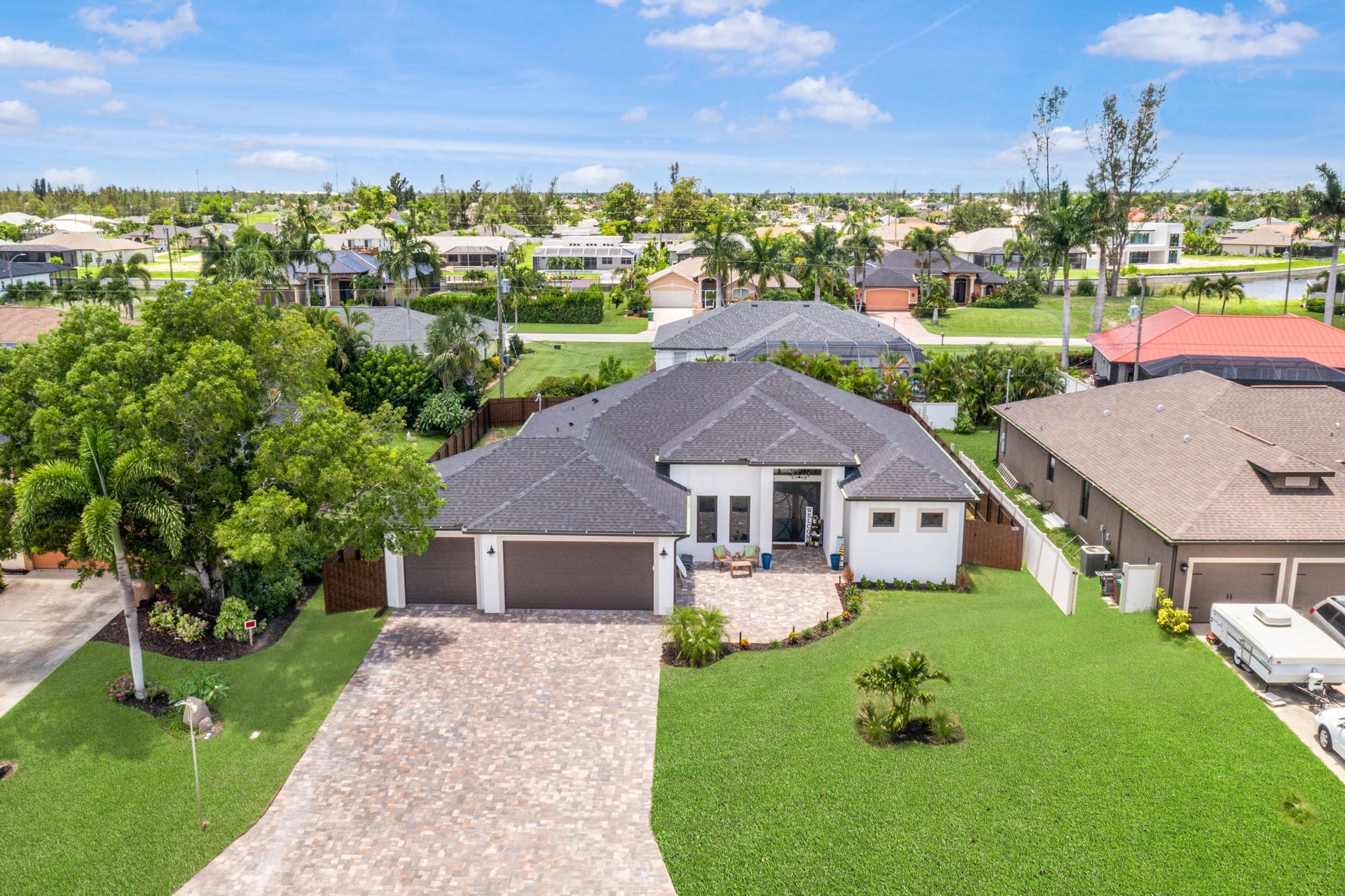 Aerial view of a modern house with a dark roof and driveway, surrounded by green lawns and other homes.
