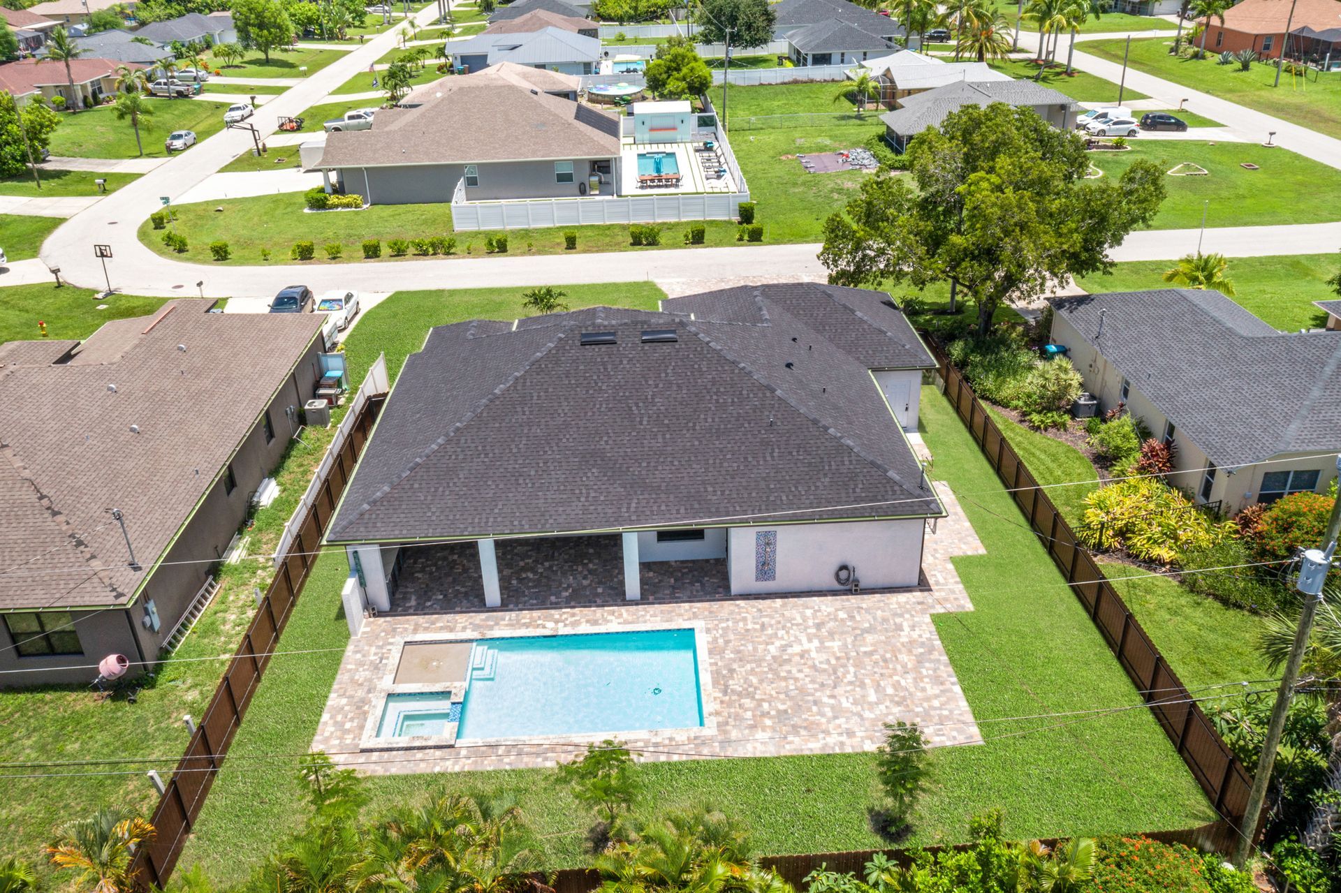 Aerial view of a beige house with a dark roof, pool, and green lawn surrounded by a wooden fence.