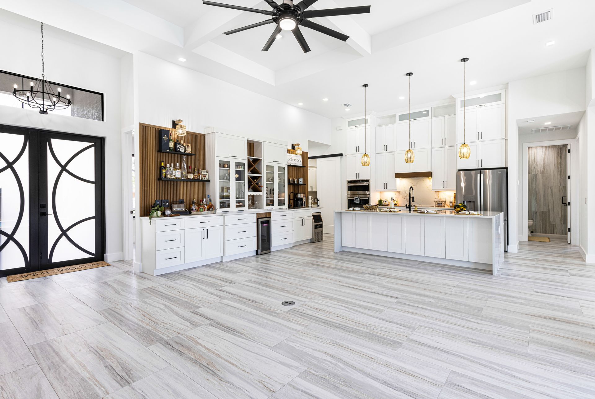 Spacious, white modern kitchen with island, cabinets, and stainless steel appliances. Wooden floors and black doors.