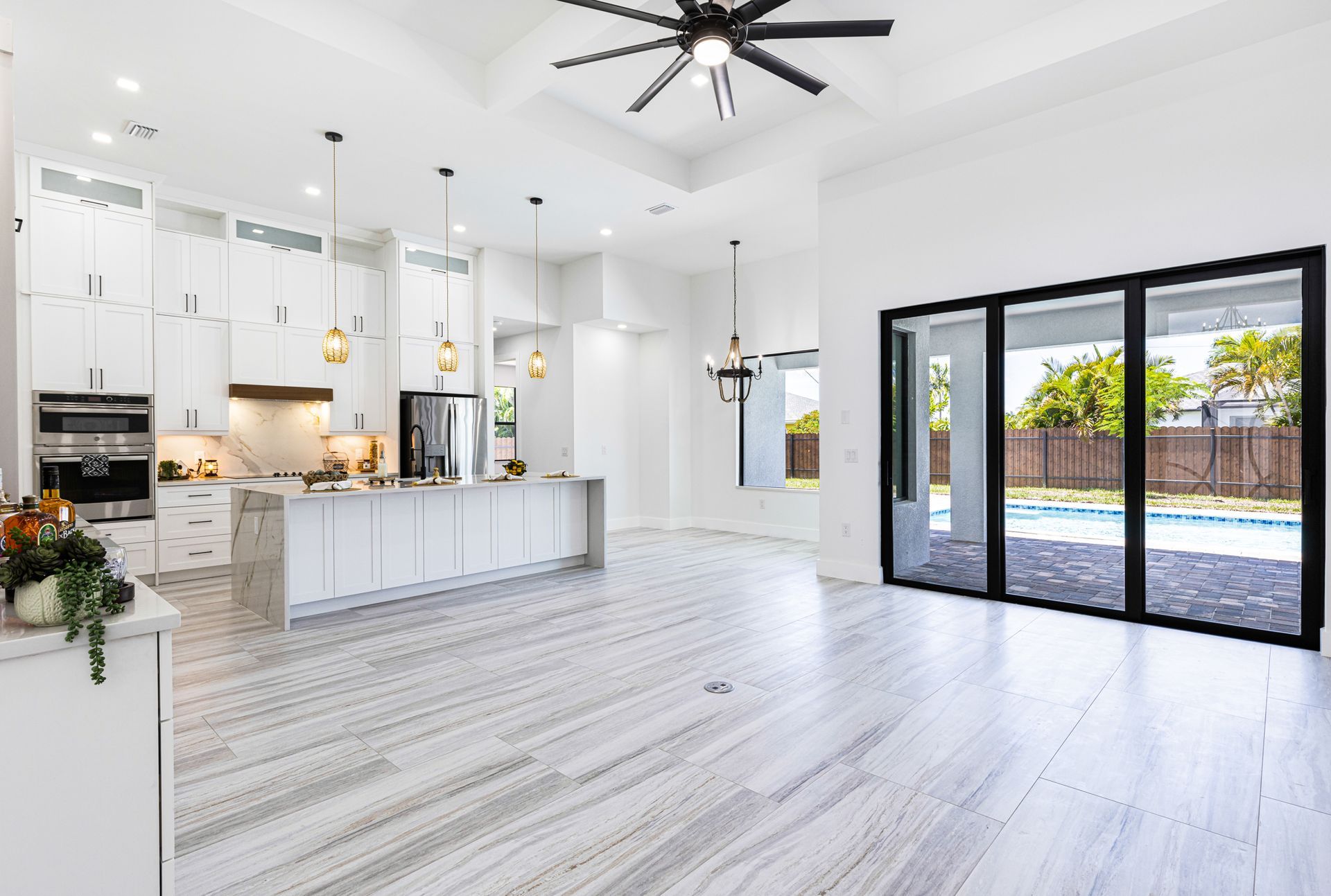 Spacious white kitchen with marble floors and a view to a pool.