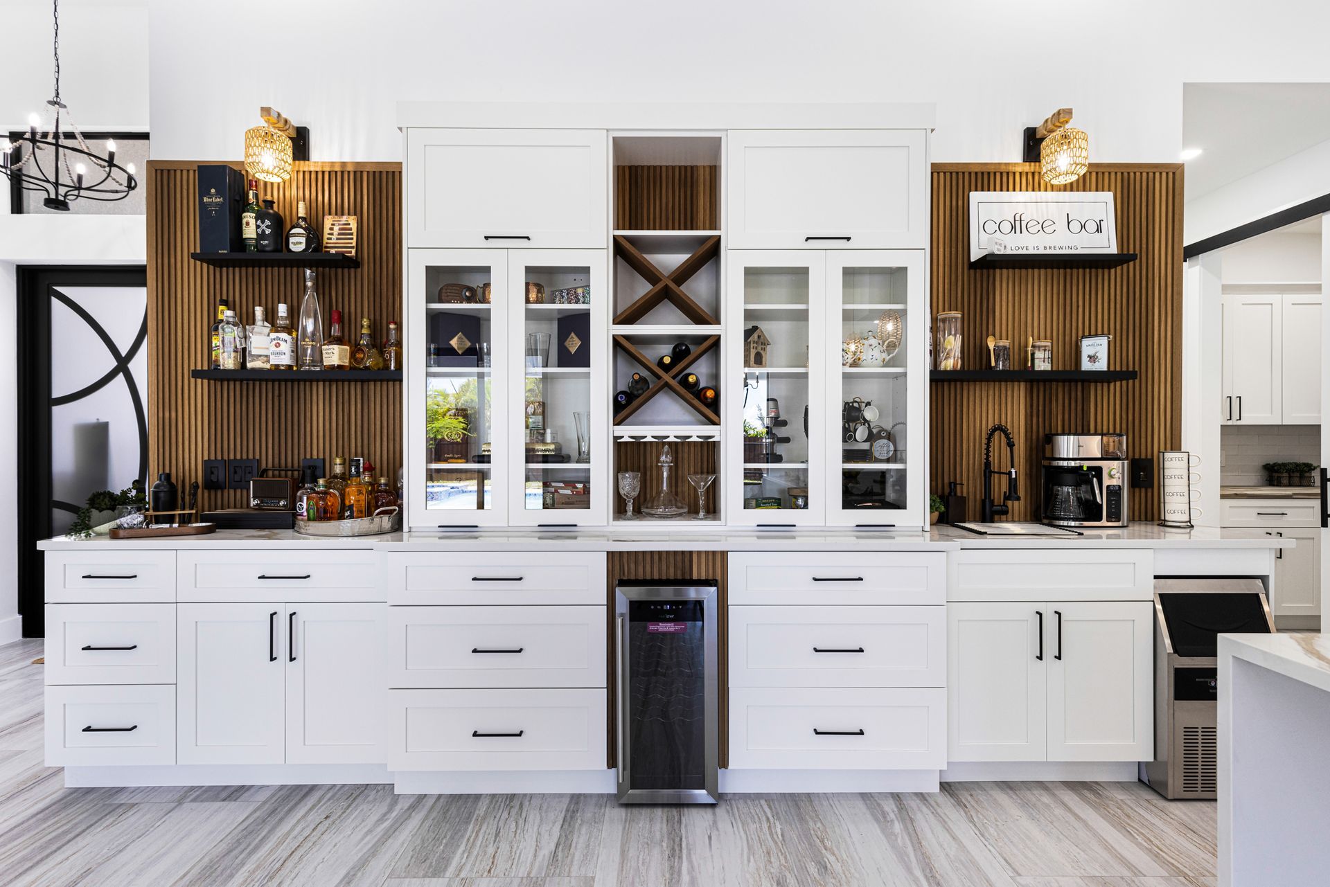 White bar cabinet with liquor, glasses, and a wine cooler set against wood paneling.