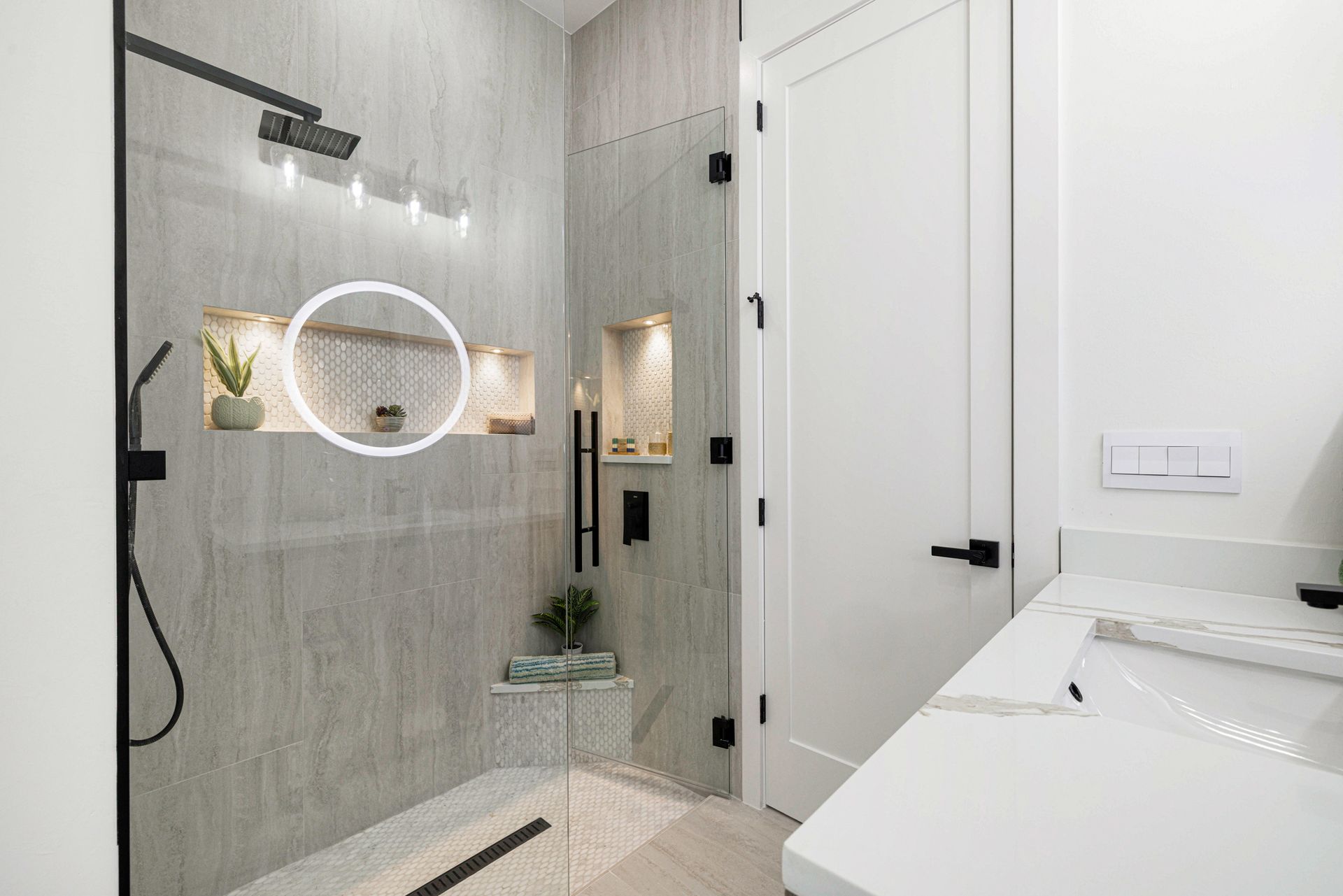 Modern shower with gray tile, black fixtures, recessed shelves, and white door.
