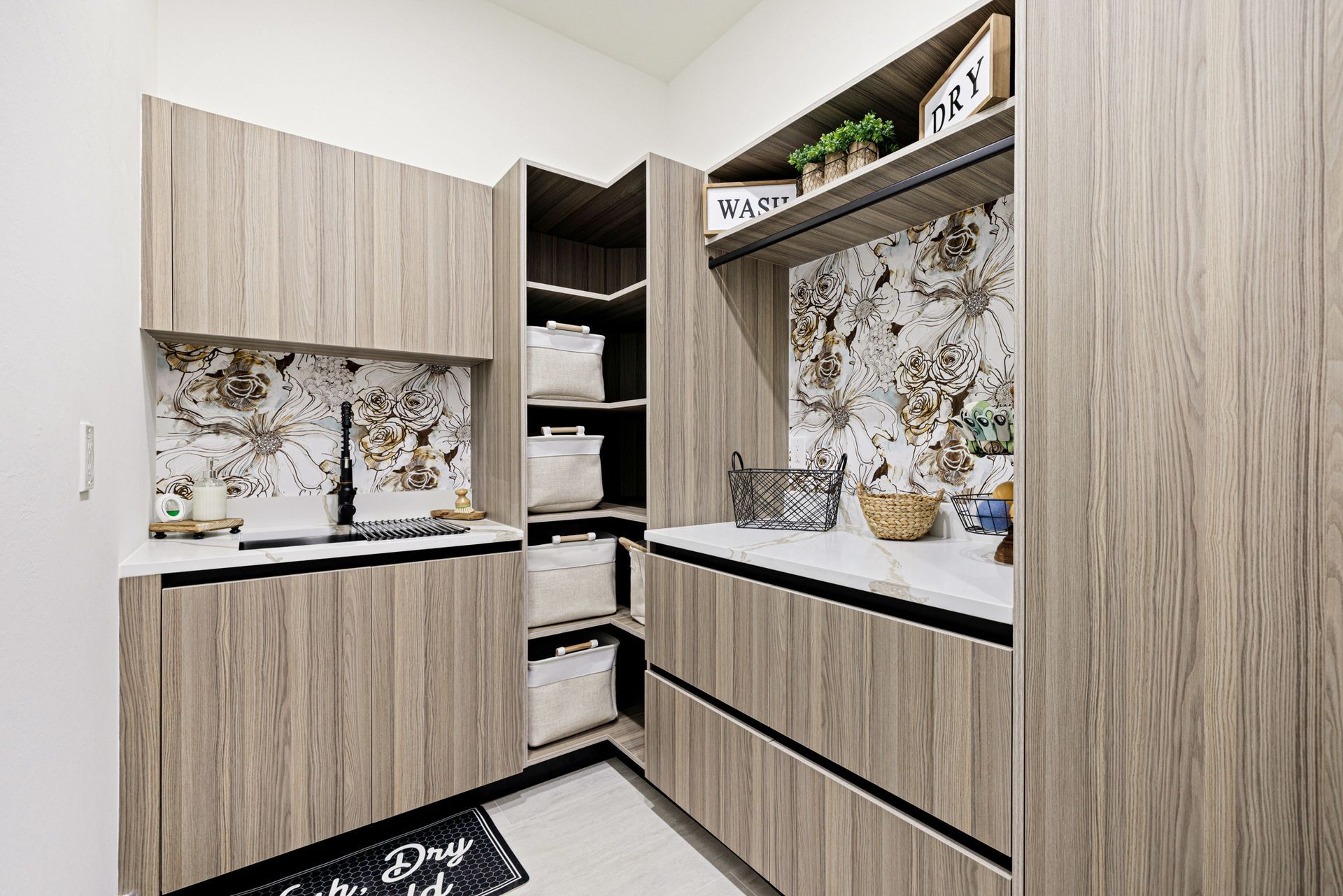 Laundry room with wood-grain cabinets, floral wallpaper, white countertop, and baskets.