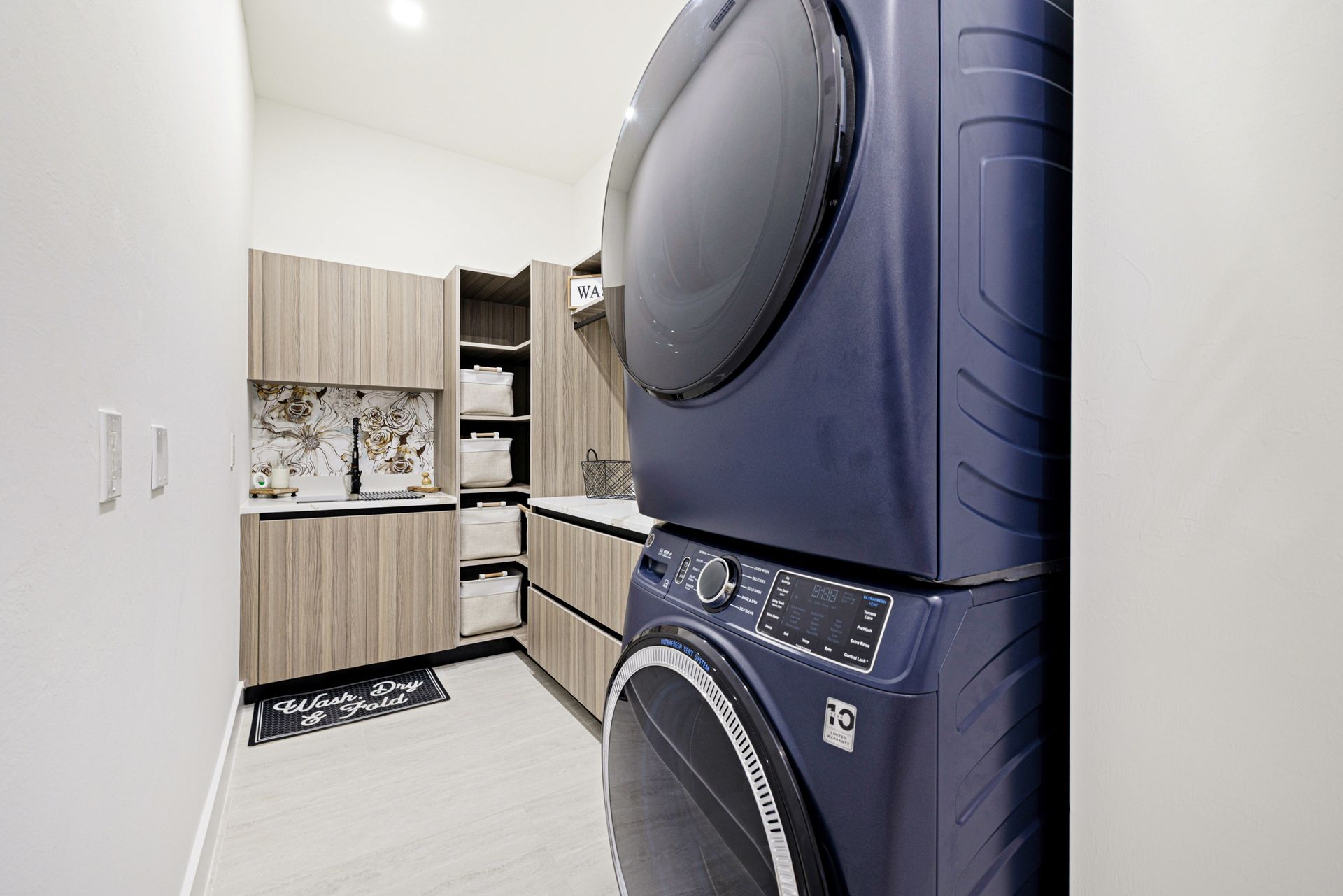 Stacked blue washer and dryer in a laundry room with light wood cabinets and white walls.
