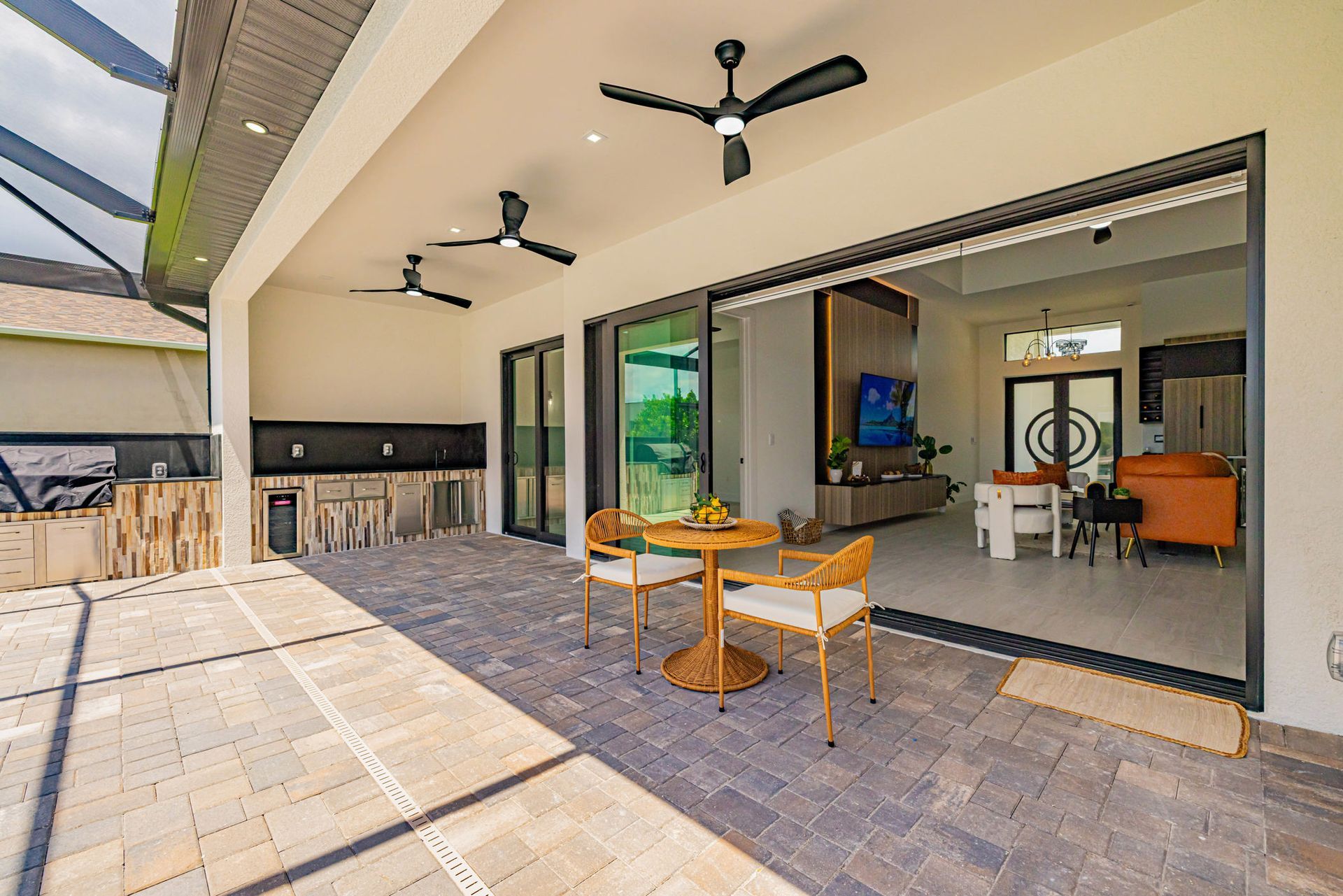 Patio with outdoor kitchen, open doors to living room, two chairs, table.