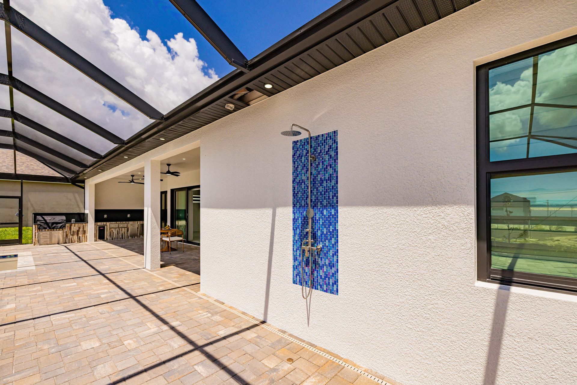 Outdoor shower with blue tile on a stucco wall, under a patio with a dark glass window.