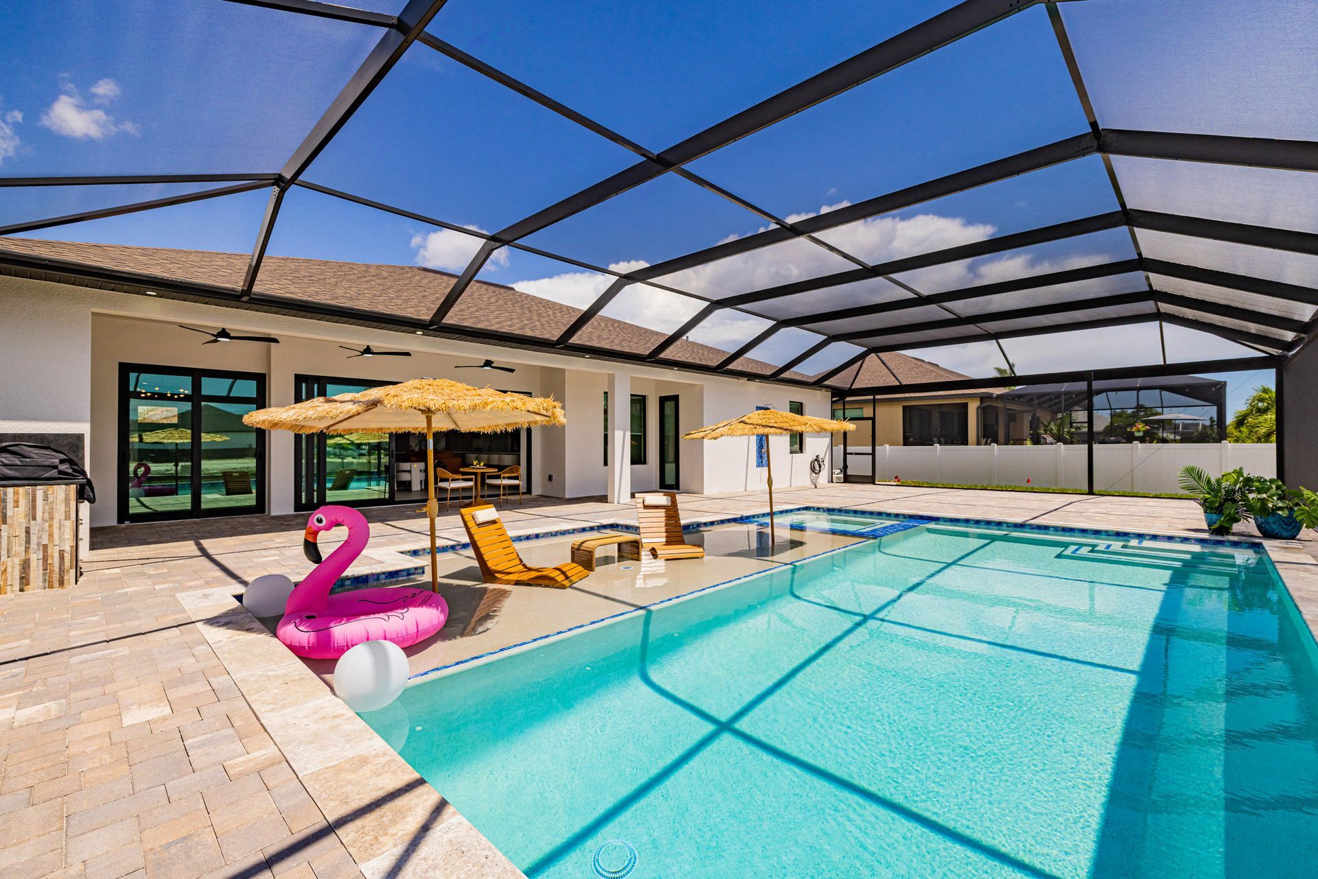 Pool area with turquoise water, patio furniture, and flamingo float under a screened enclosure.