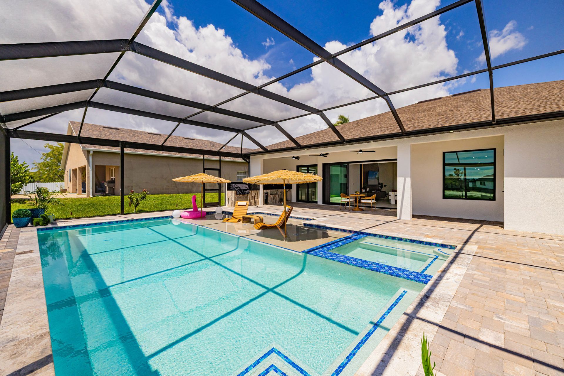 Pool and spa in a screened-in patio of a house, sunny day with lounge chairs and umbrella.
