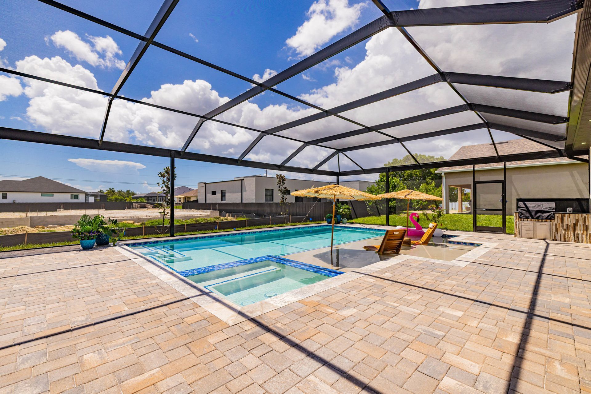Pool area with covered lanai; person in chair, blue sky, brick patio.