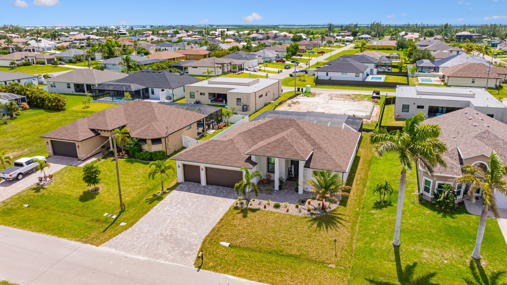 Aerial view of houses in a sunny residential neighborhood with green lawns and blue sky.