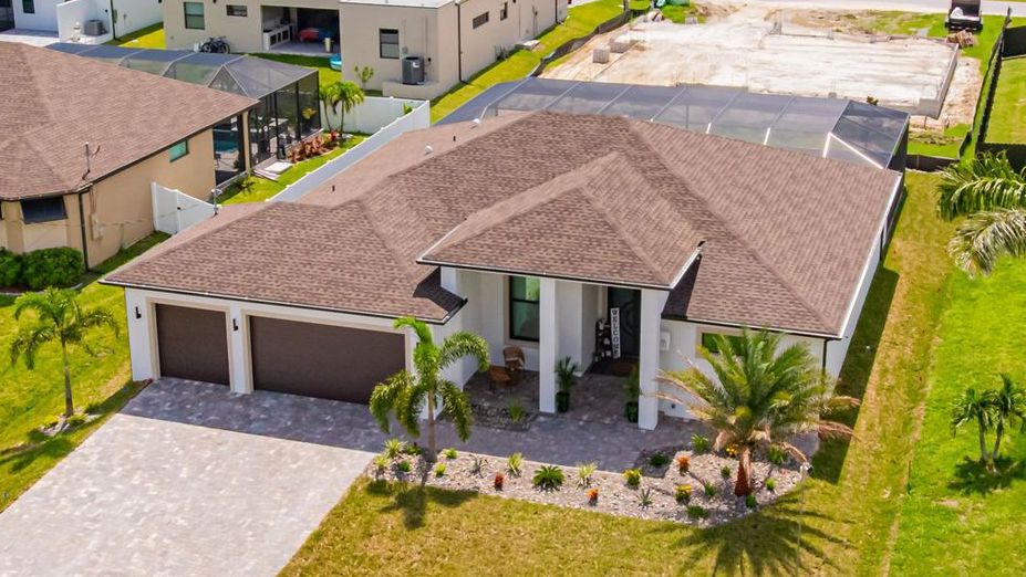 Aerial view of a modern house with brown roof, two-car garage, and landscaped yard.